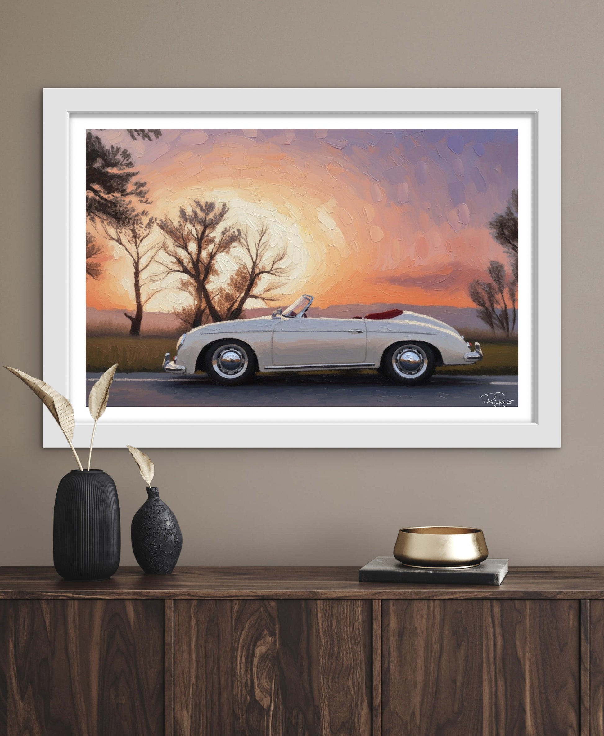 Framed artwork of a vintage car at sunset on a wall above a wooden console table.