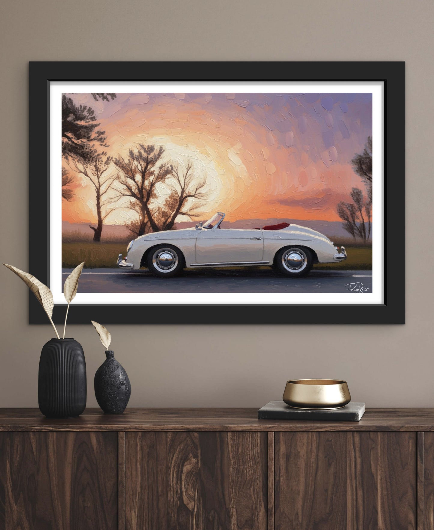 Framed artwork of a vintage car at sunset on a wall above a wooden console table.