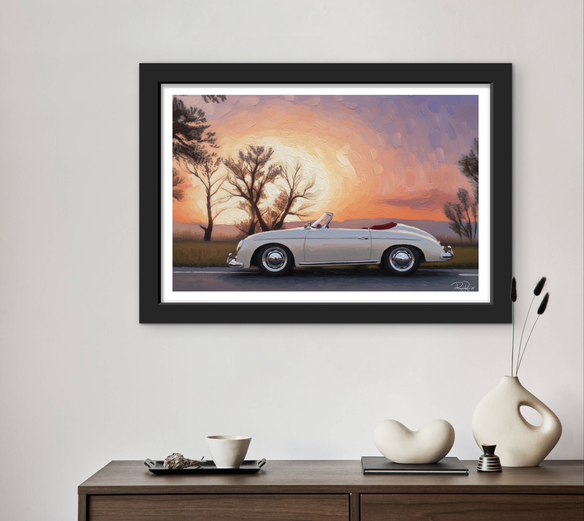 Framed artwork of a classic car at sunset on a wall above a wooden console table with decorative items.