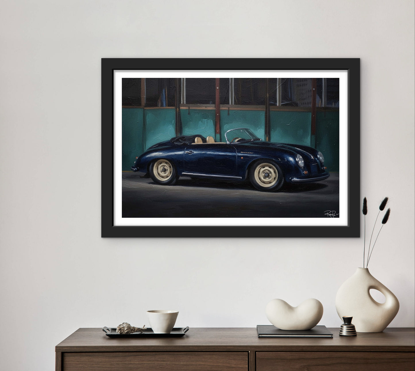 Framed artwork of a vintage car on a wall above a wooden console table with decorative items.