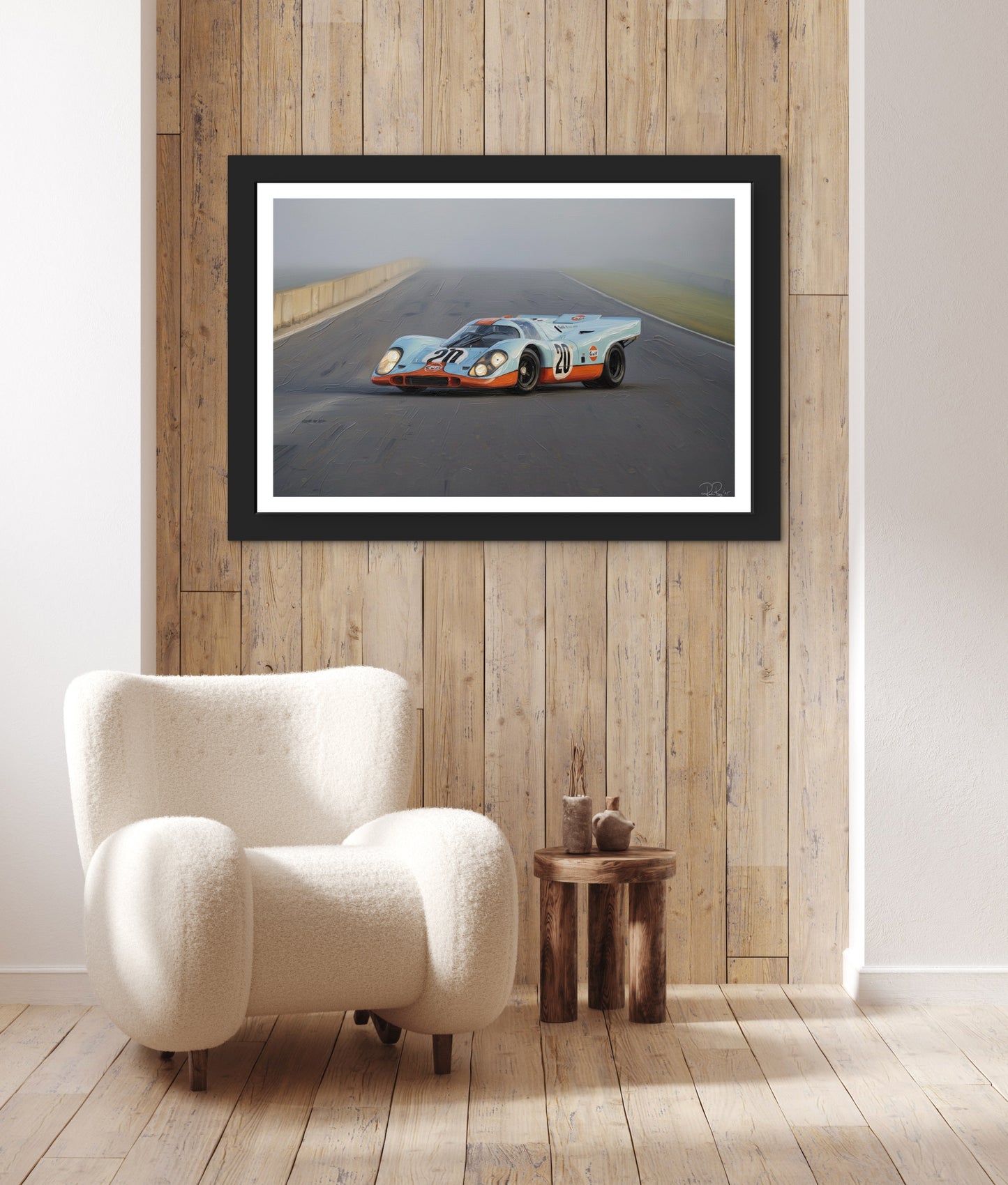 Framed artwork of a race car on a wall above a white armchair in a room with wooden flooring and wall.