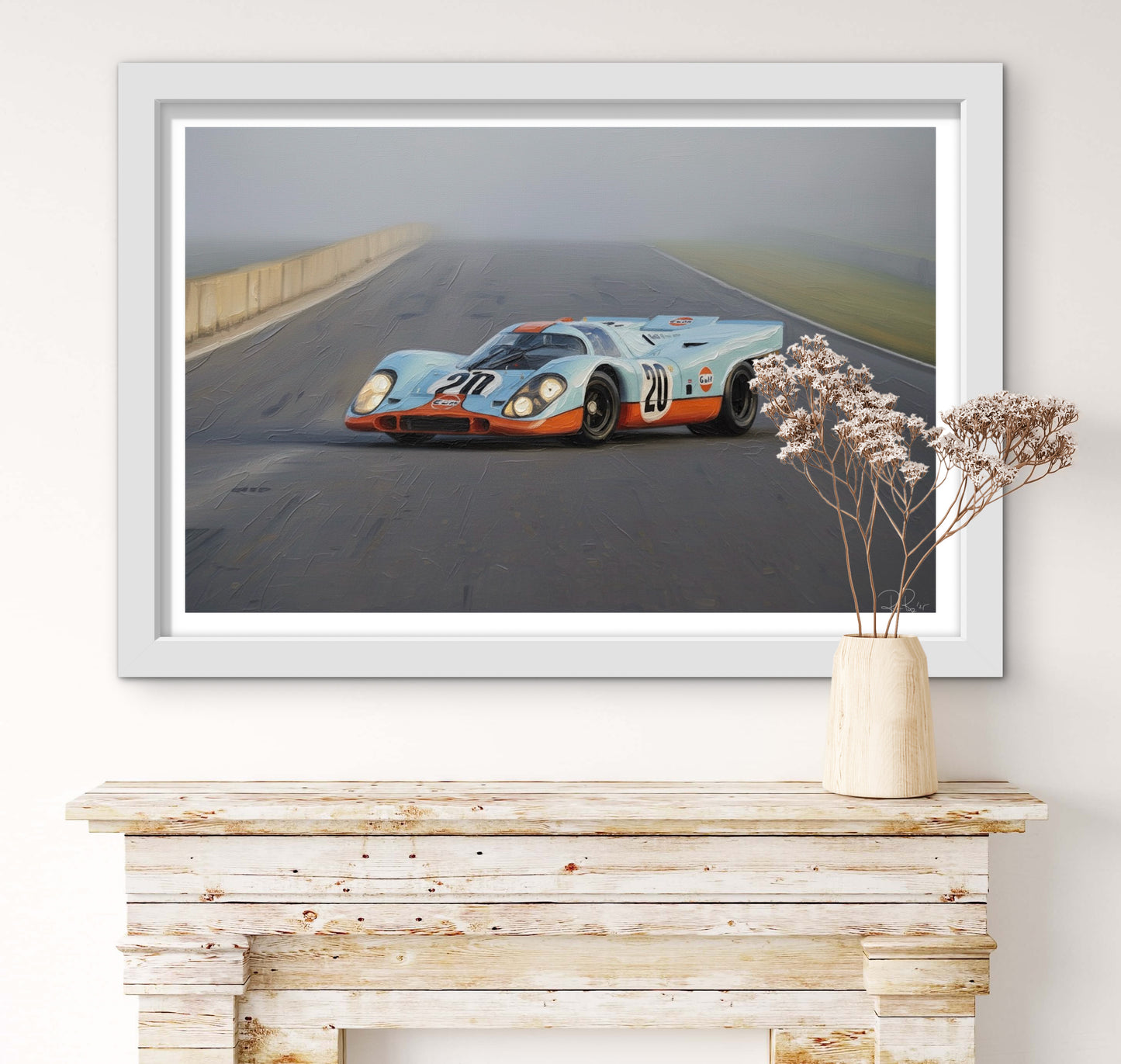 Framed picture of a race car on a road above a wooden console table with a vase.