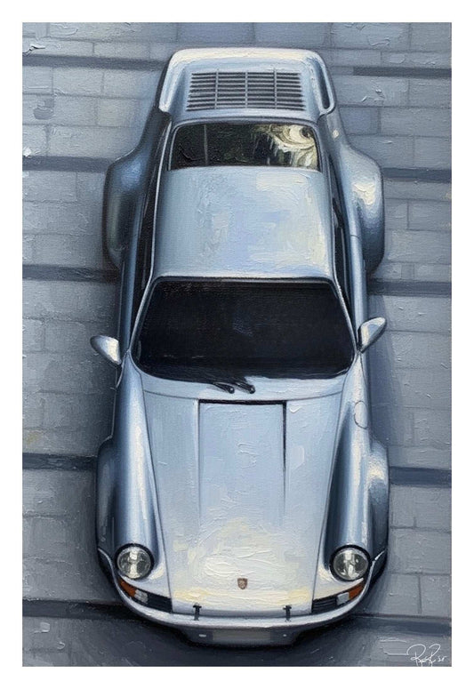 Top-down view of a silver sports car against a gray brick wall.