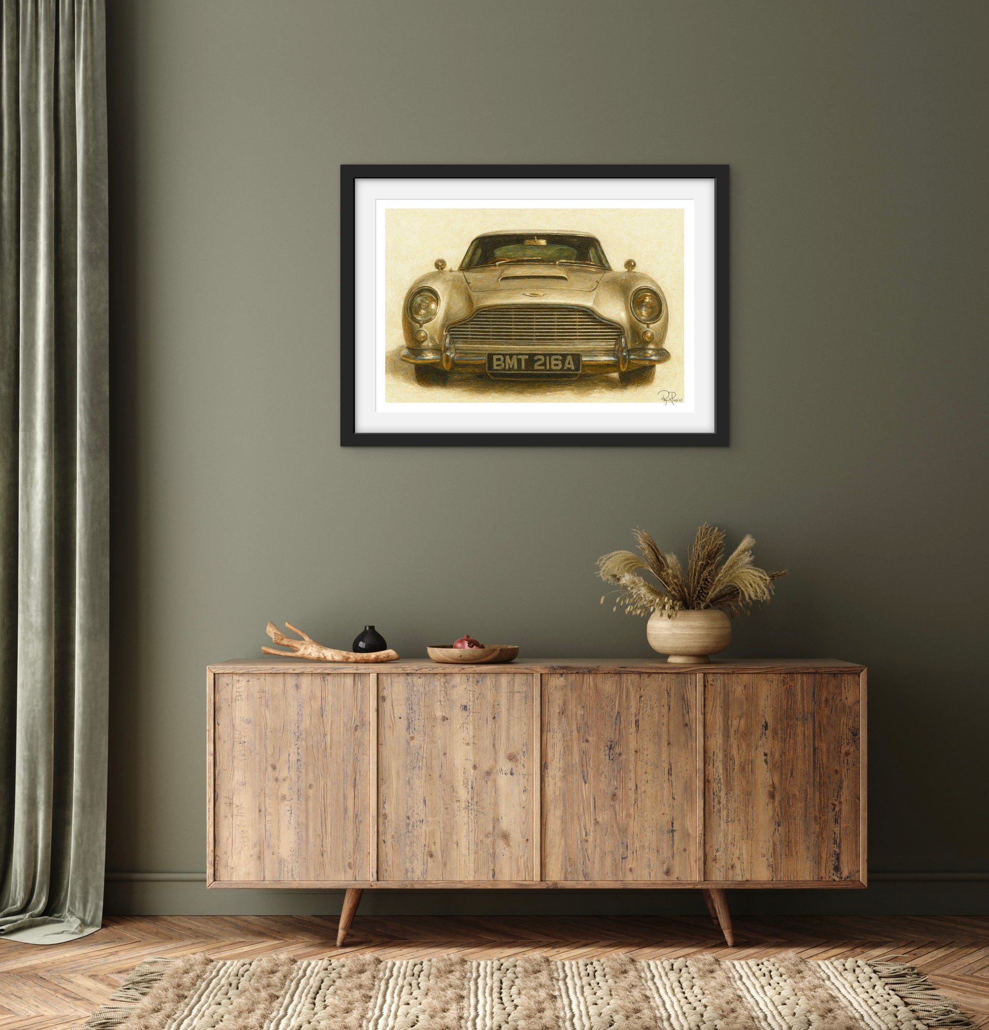 Framed picture of a vintage car on a wall above a wooden sideboard.
