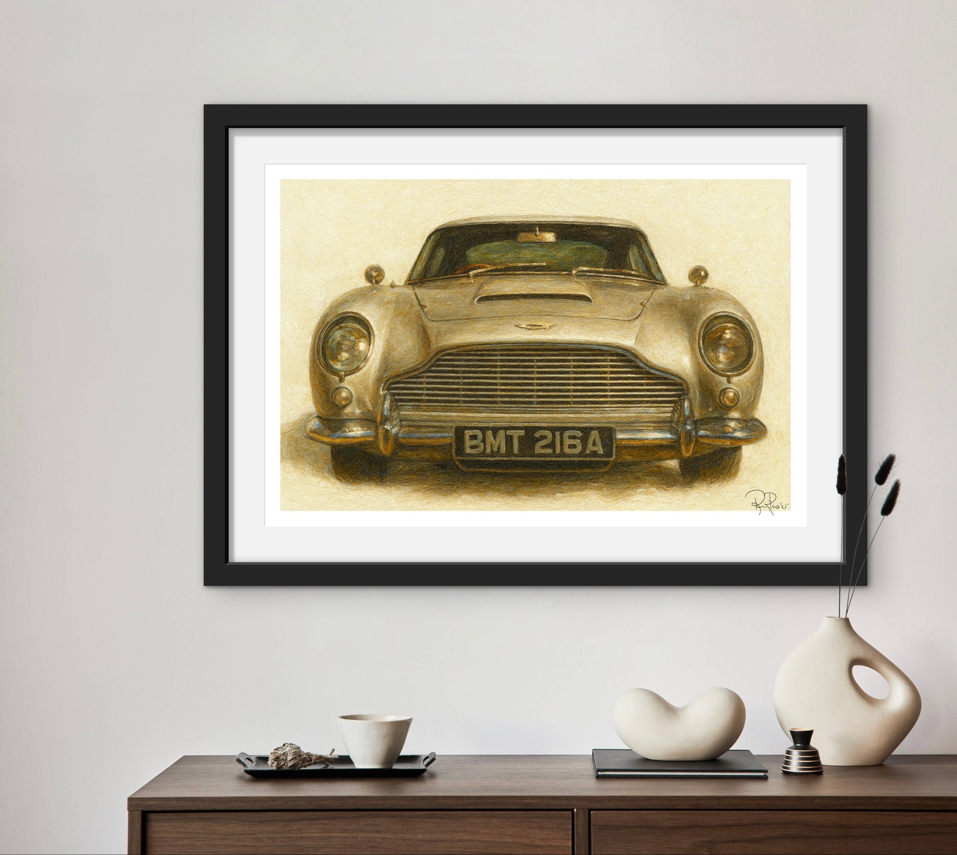 Framed artwork of a vintage car on a wall above a wooden console table with decorative items.