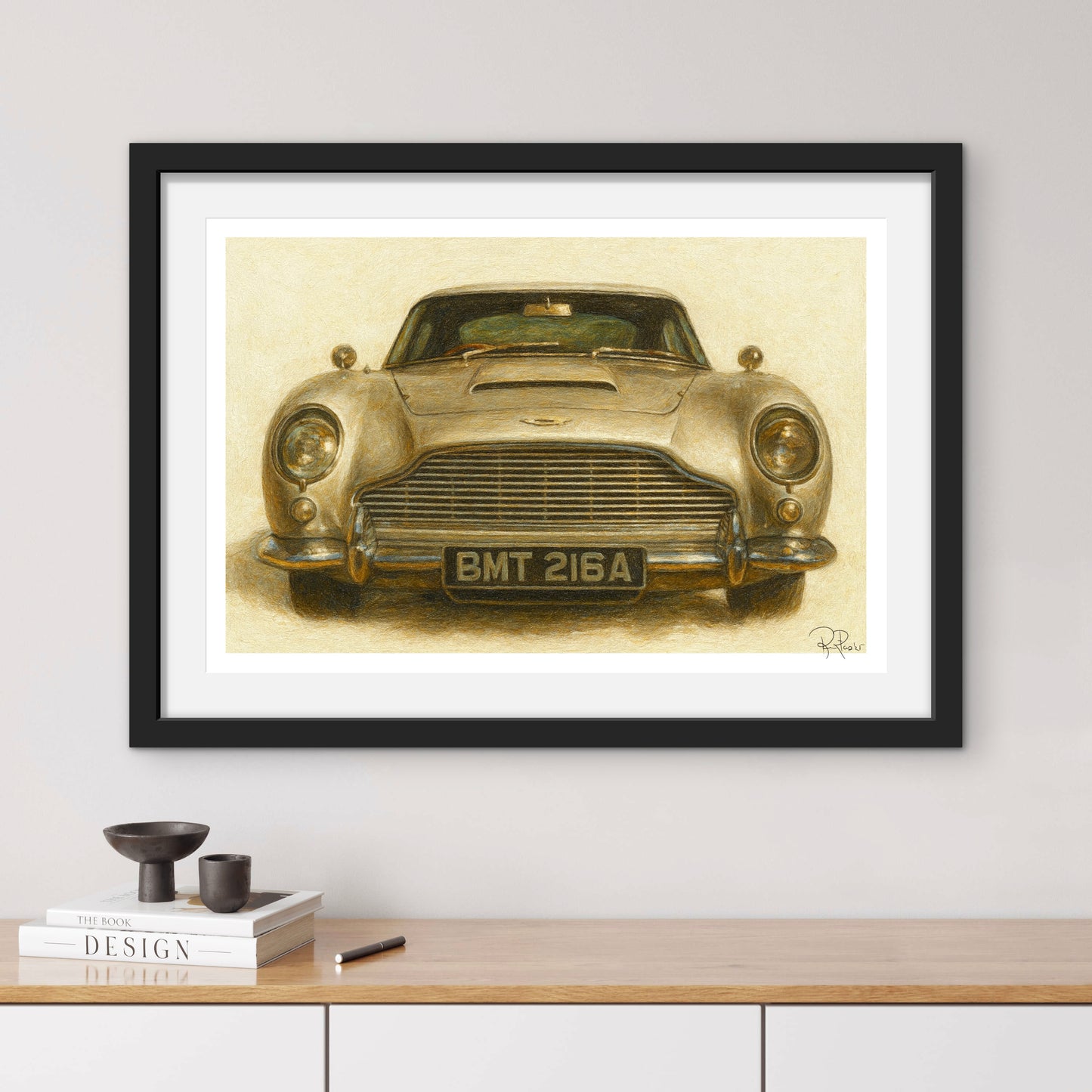 Framed artwork of a vintage car on a wall above a wooden shelf.