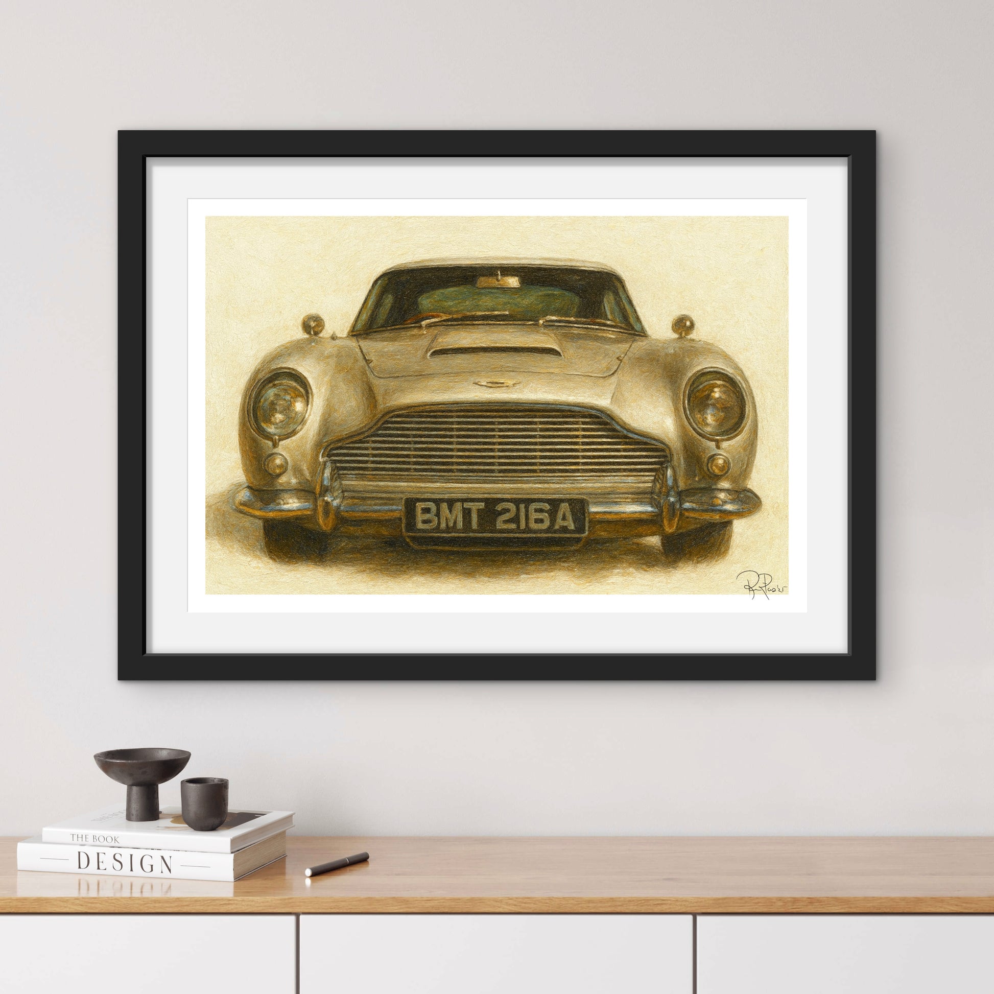 Framed artwork of a vintage car on a wall above a wooden shelf.