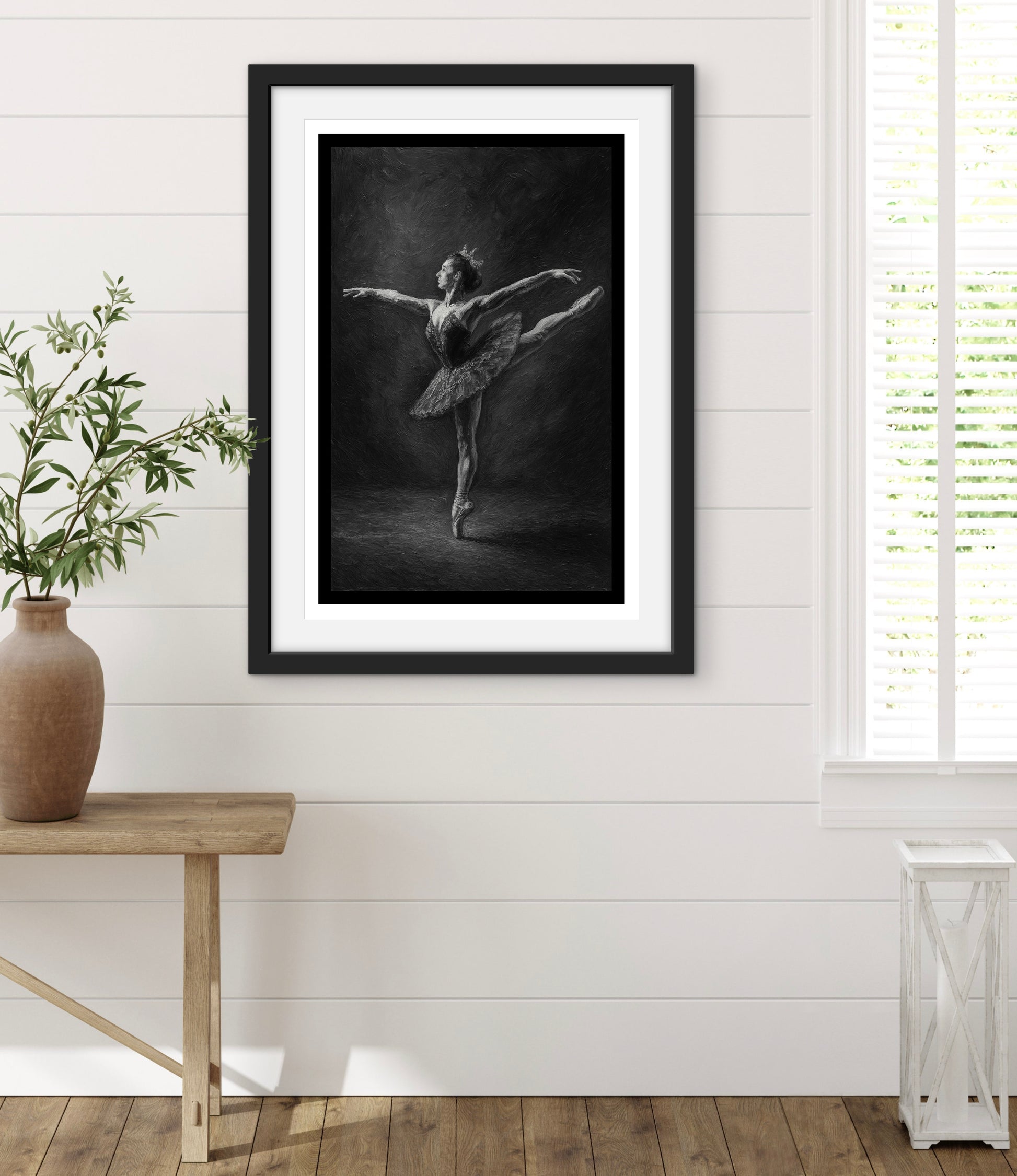 Framed black and white ballet dancer print on a wall with a wooden table and plant.