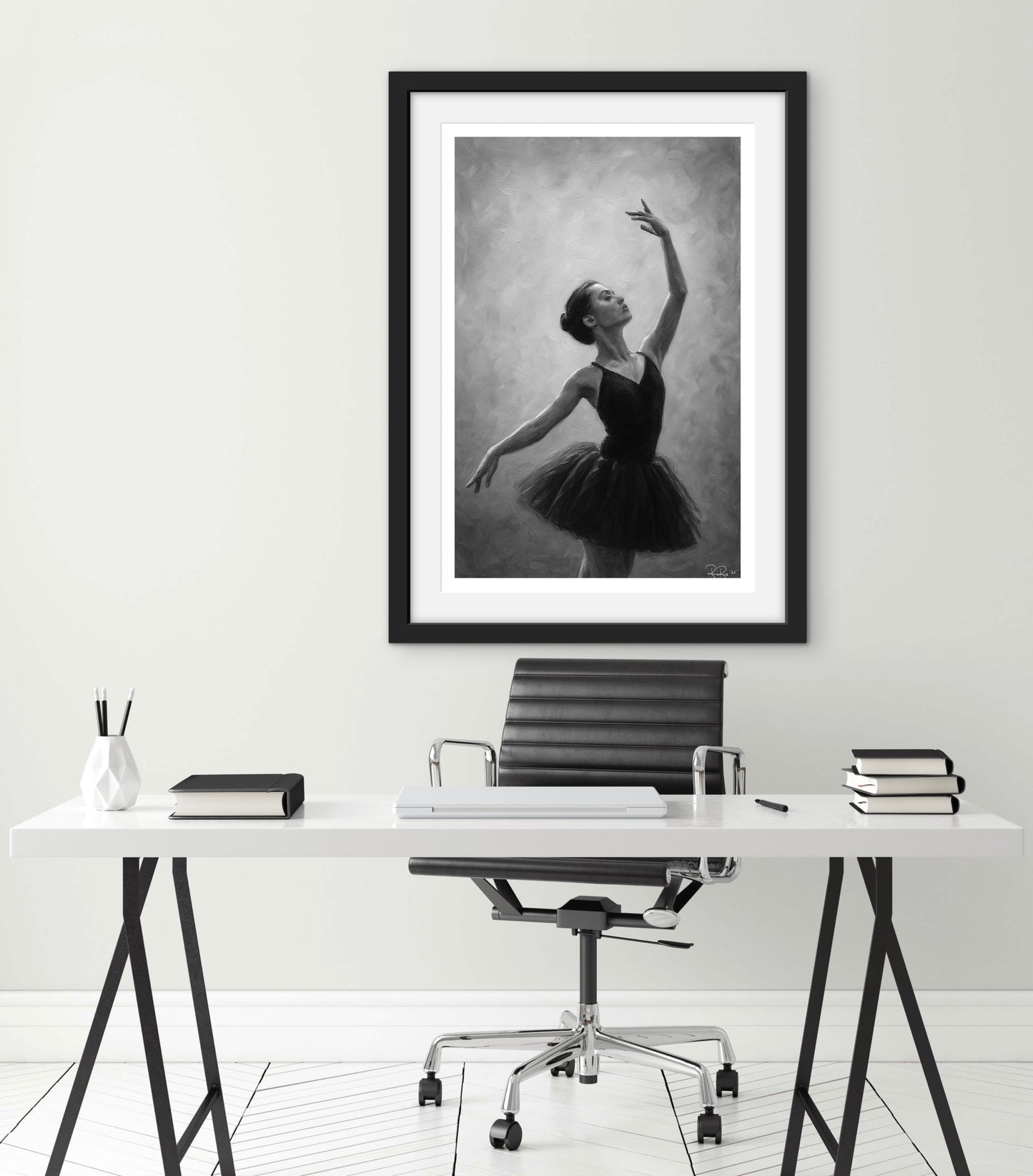 Framed black and white artwork of a dancer above a desk with office supplies.