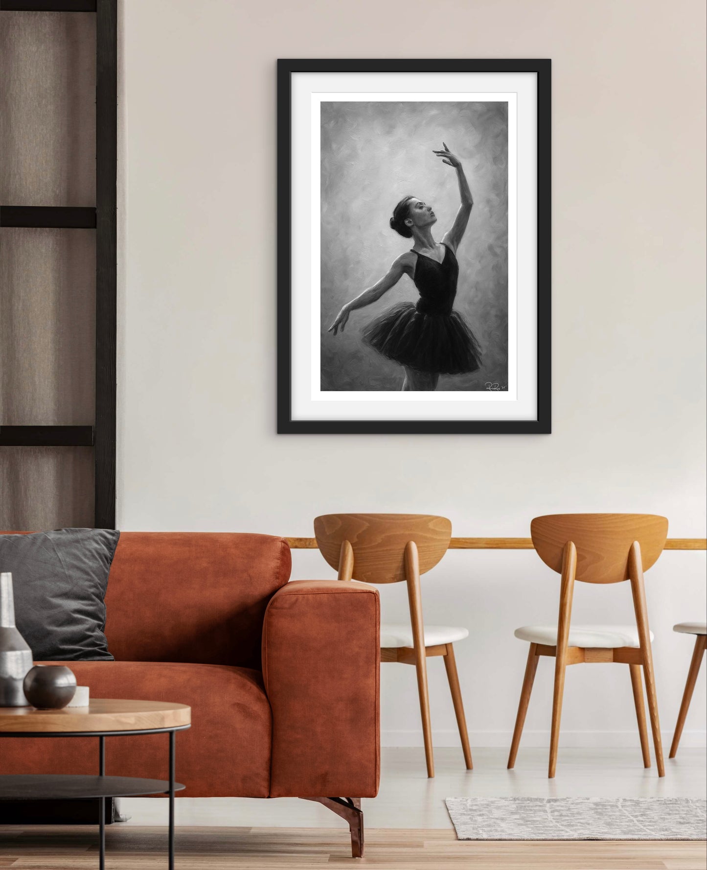 Framed black and white artwork of a dancer in a living room setting with a brown sofa and wooden chairs.