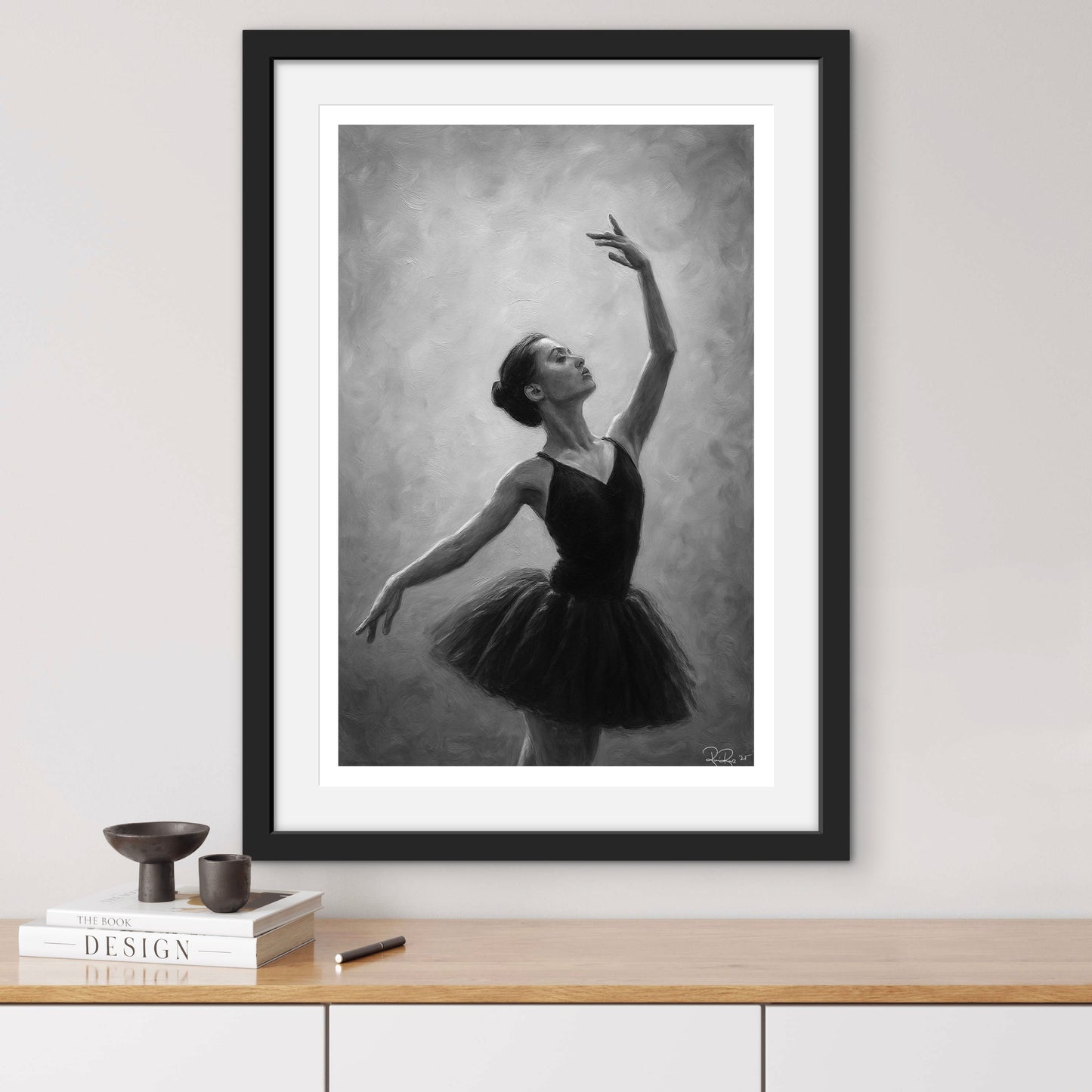 Framed artwork of a ballerina in a black tutu on a white wall above a wooden shelf.