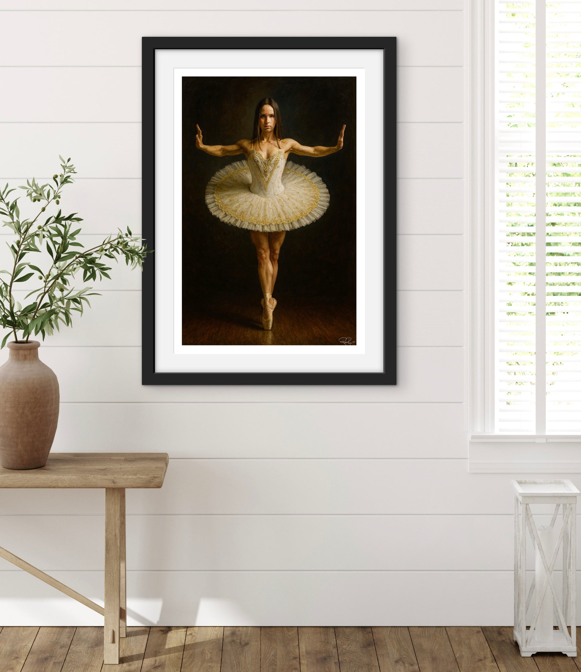 Framed artwork of a ballerina in a tutu on a white wall with a wooden floor.