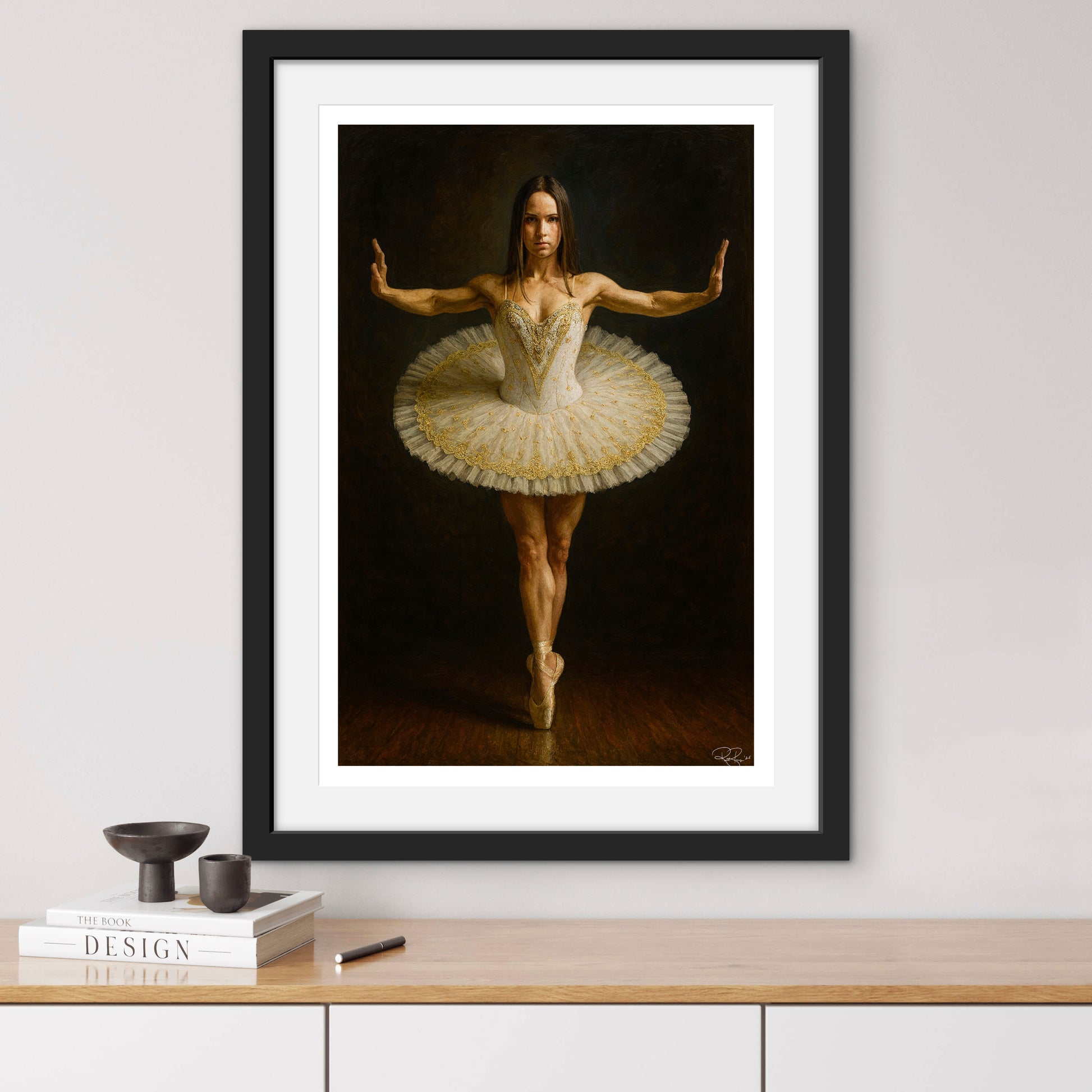 Framed artwork of a ballerina in a tutu on a wall above a wooden surface.