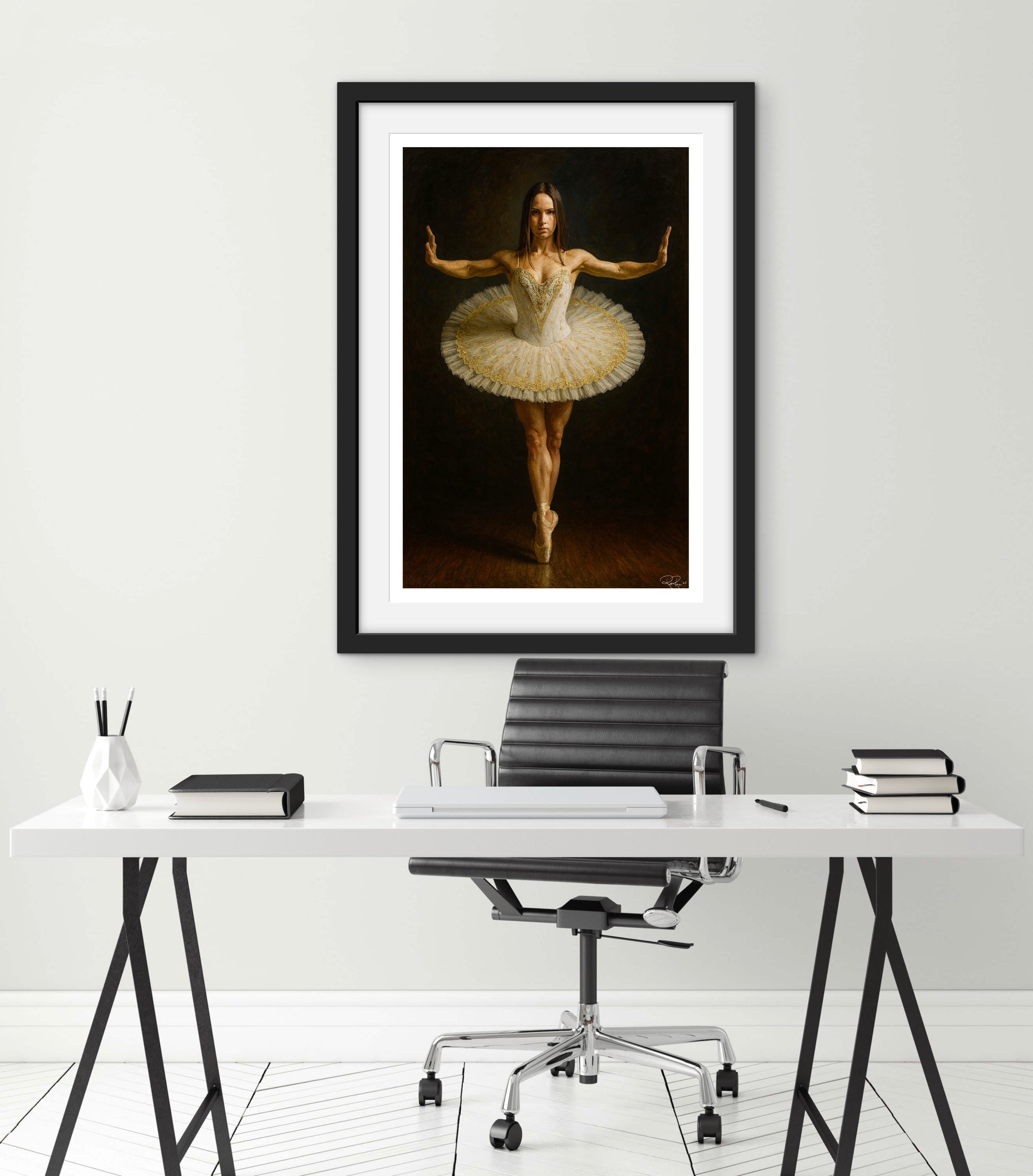 Framed artwork of a ballerina in a tutu on a white wall above a desk.