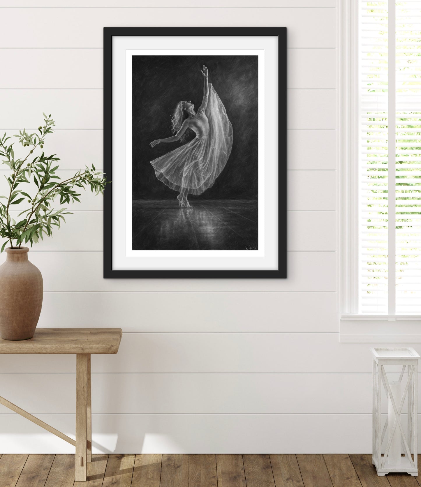 Framed black and white art print of a dancer in a room with a wooden table and plant.