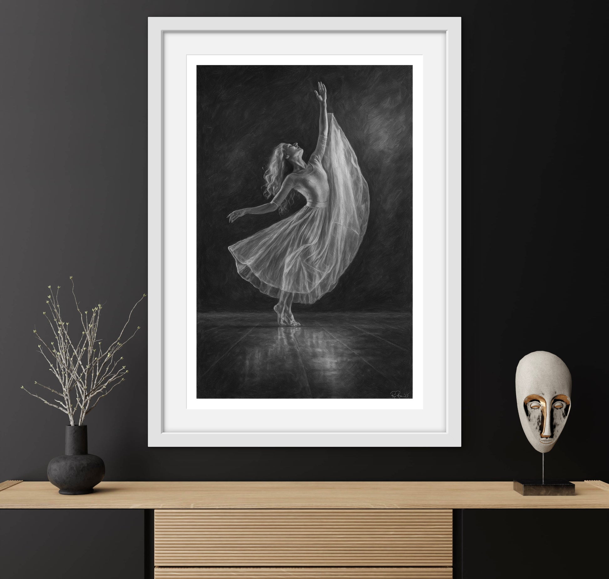 Framed black and white artwork of a dancer on a dark wall with decorative items below.