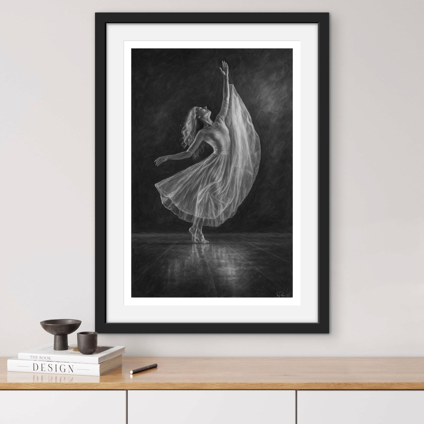 Framed black and white artwork of a dancer on a wall above a wooden shelf.