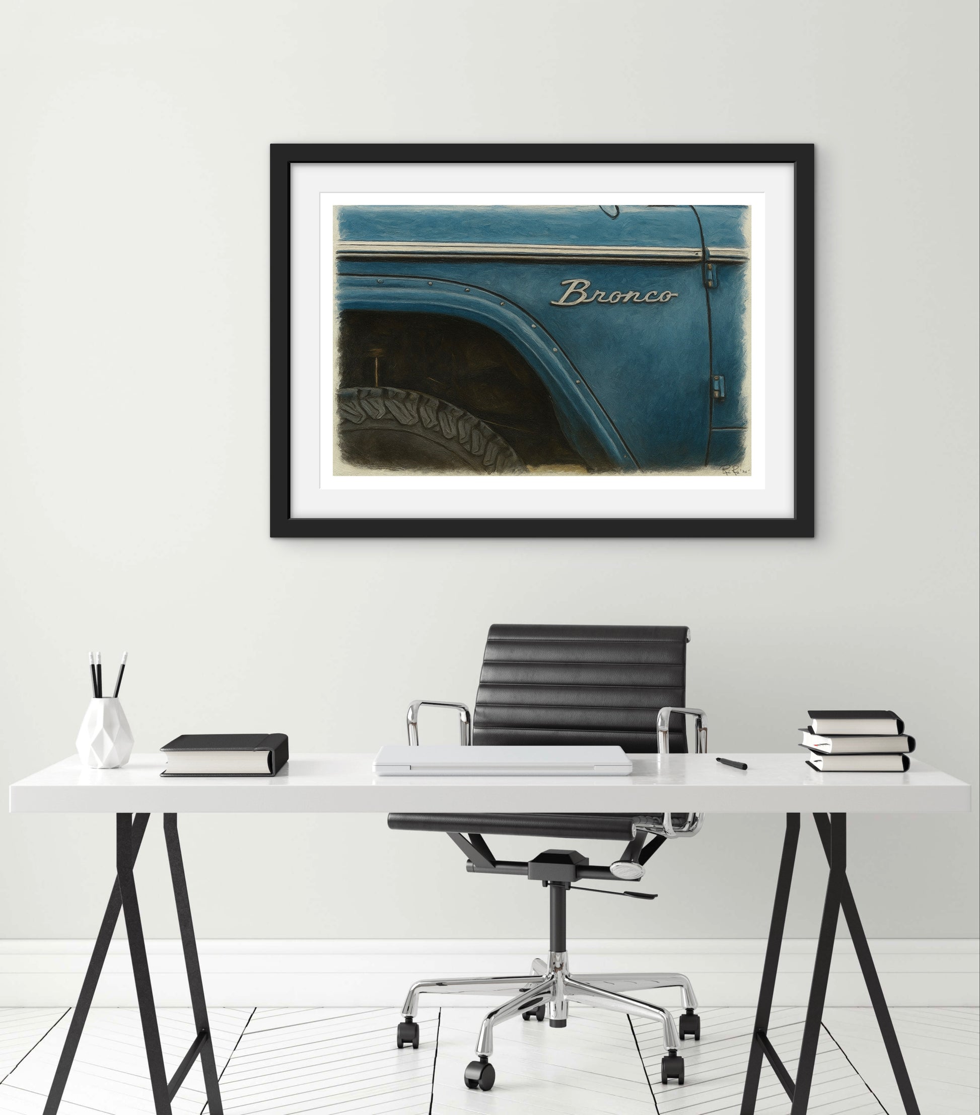 Framed photograph of a blue Bronco on a wall above a desk with office furniture.