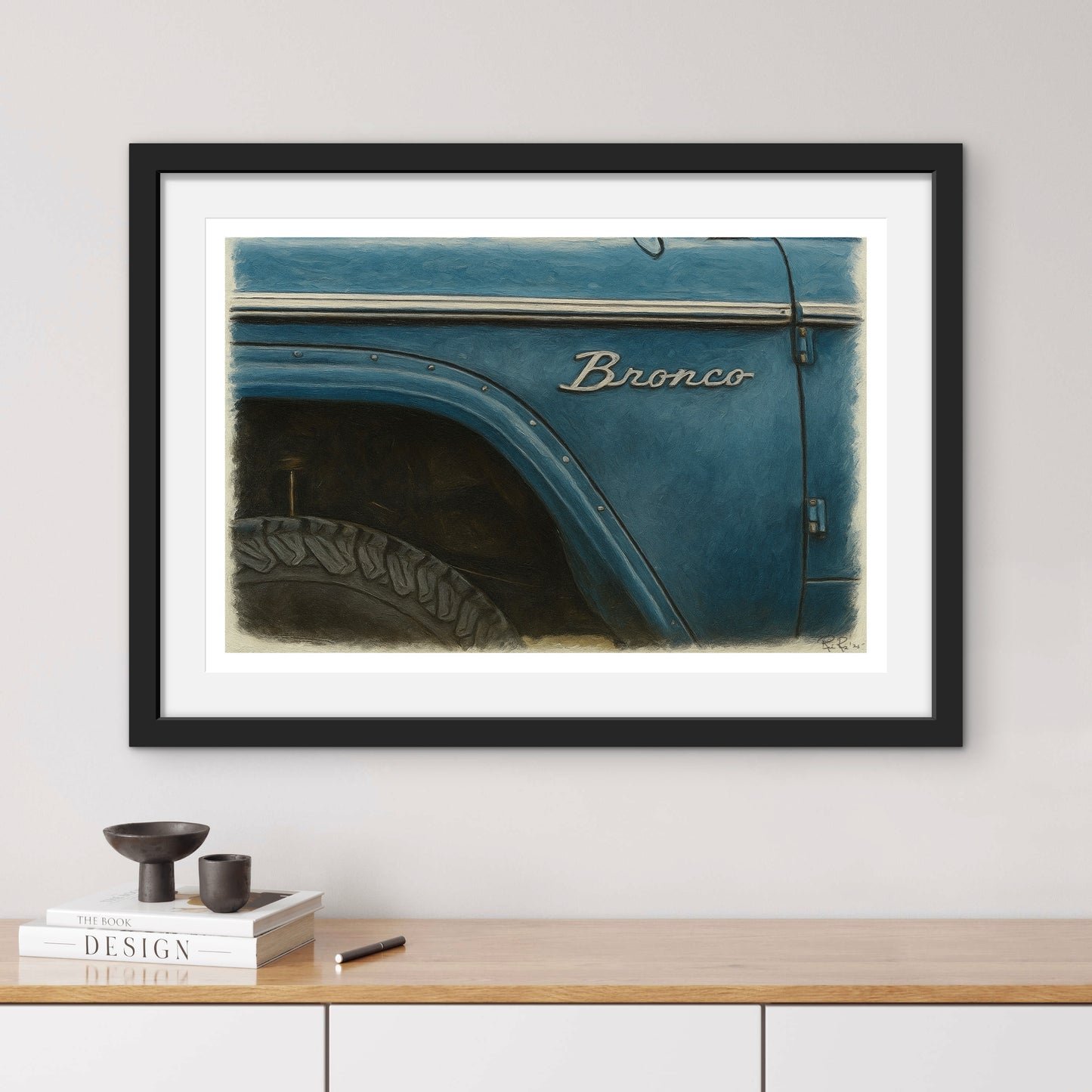 Framed artwork of a blue Ford Bronco on a wall above a wooden shelf.