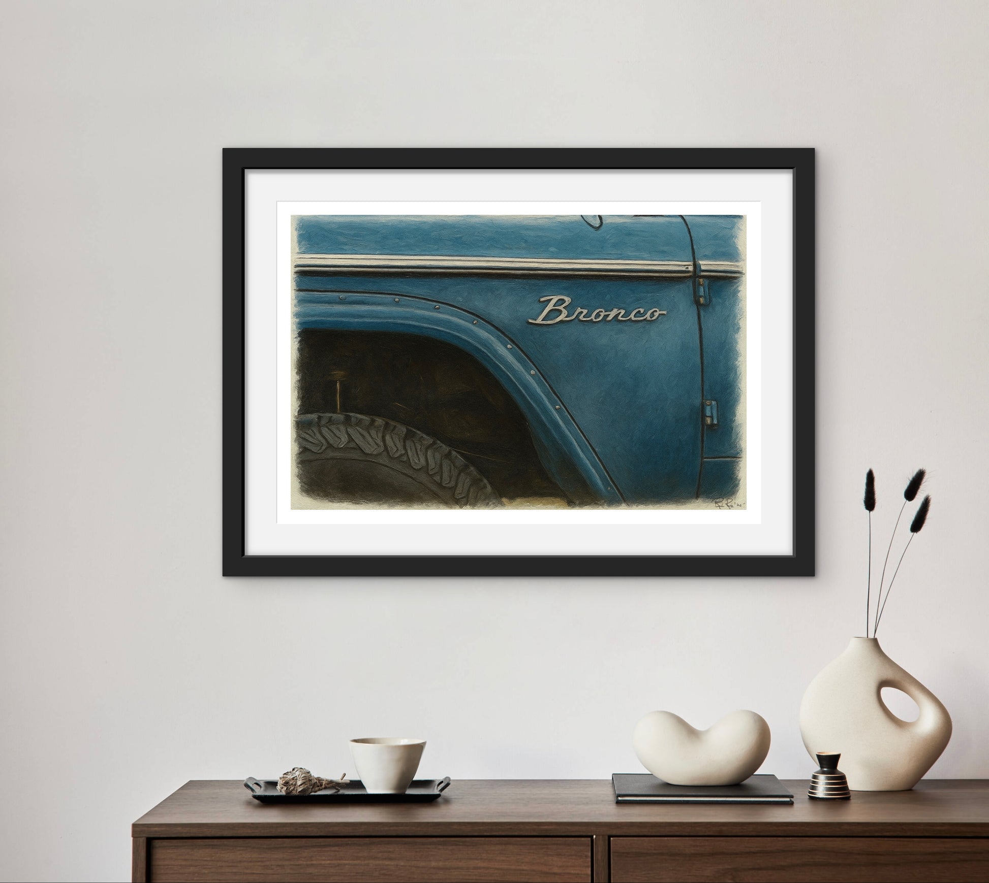 Framed picture of a blue Ford Bronco on a wall above a wooden console table with decorative items.