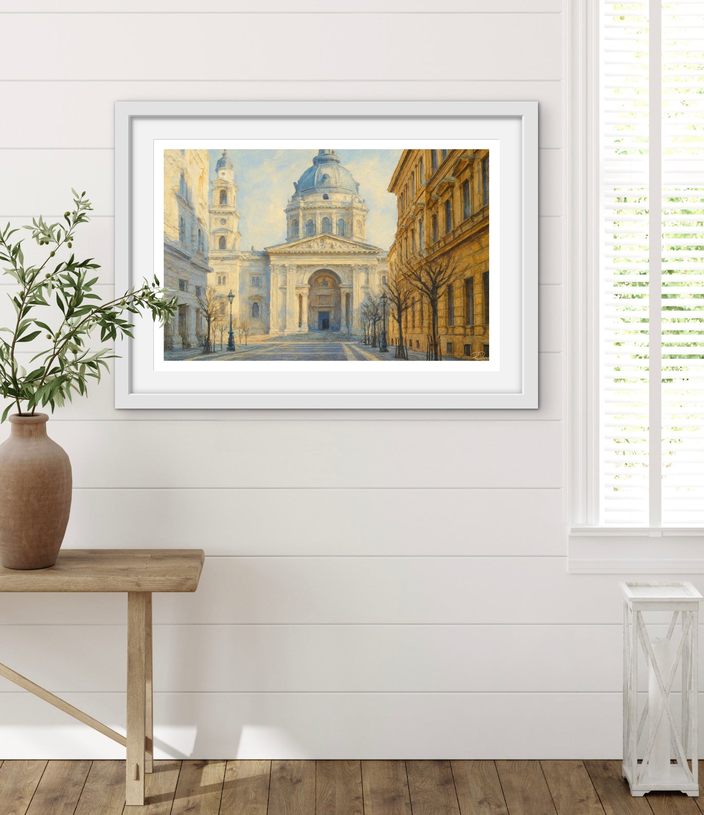 Framed artwork of a cityscape on a white wall with a wooden table and plant.