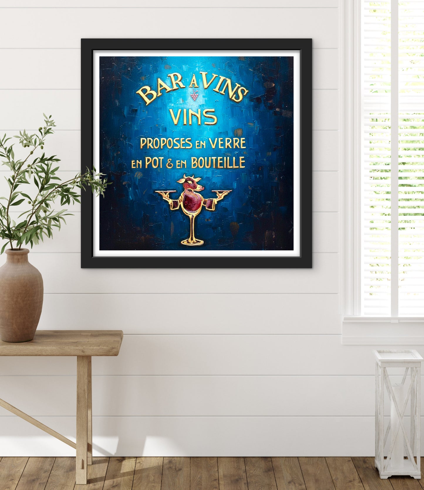 Framed vintage-style wine advertisement on a wall with a plant and table in the foreground.