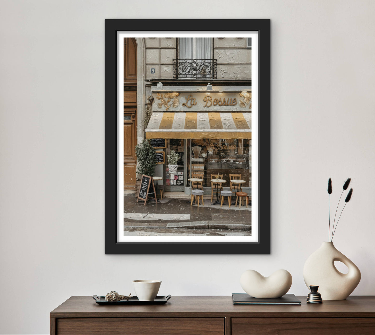 Framed photograph of a café exterior on a wall above a wooden console table with decorative items.