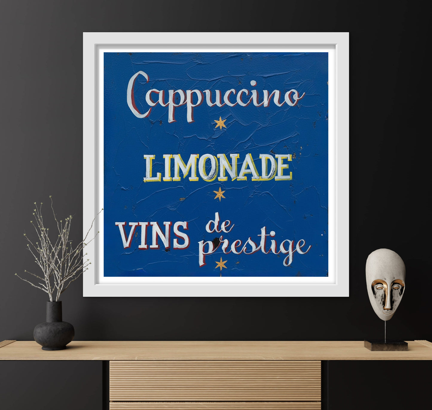 Framed artwork with text 'Cappuccino', 'Limonade', 'Vins de prestige' on a dark wall.
