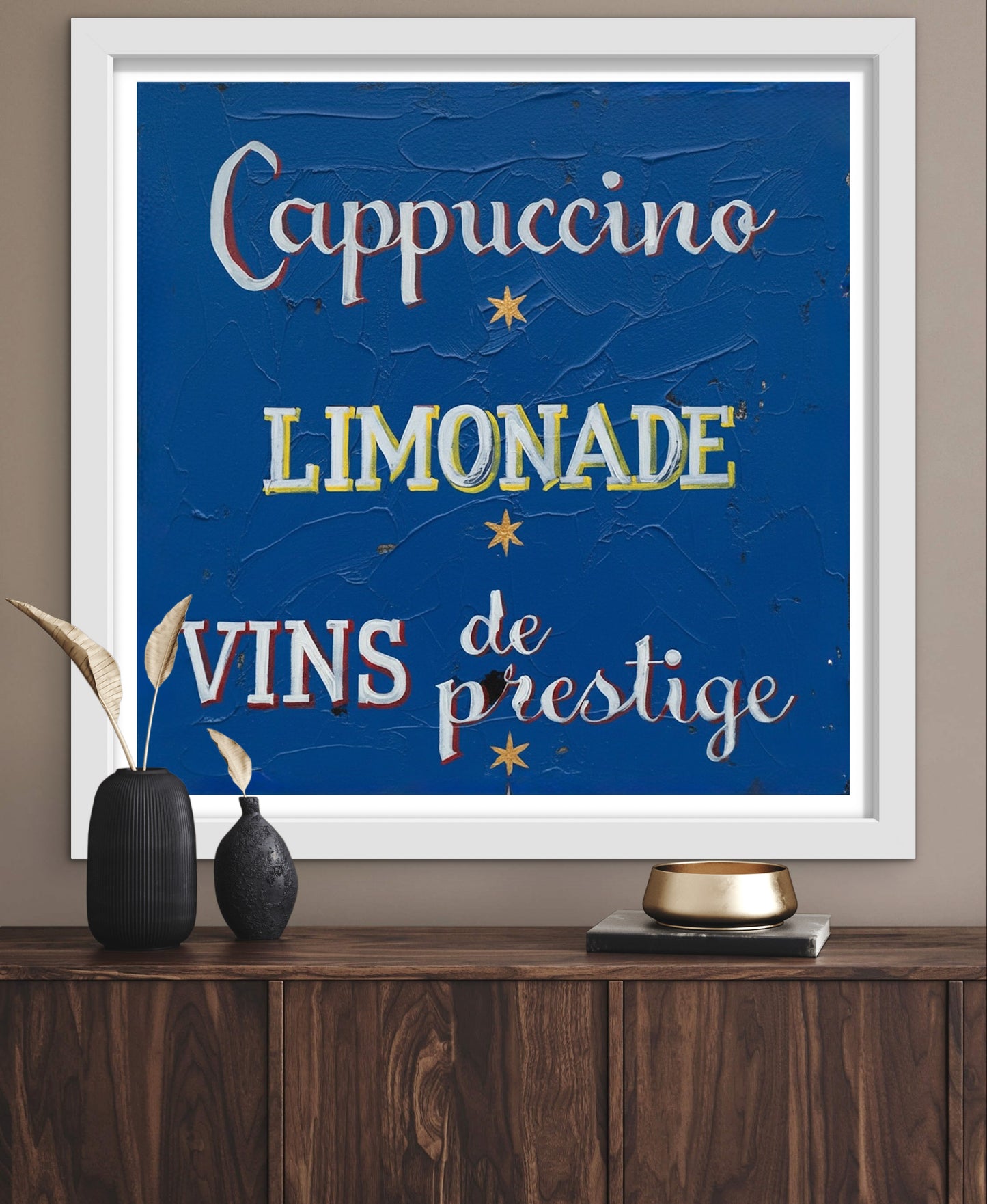 Framed artwork with text 'Cappuccino', 'Limonade', 'Vins de prestige' on a blue background, displayed on a wooden surface.