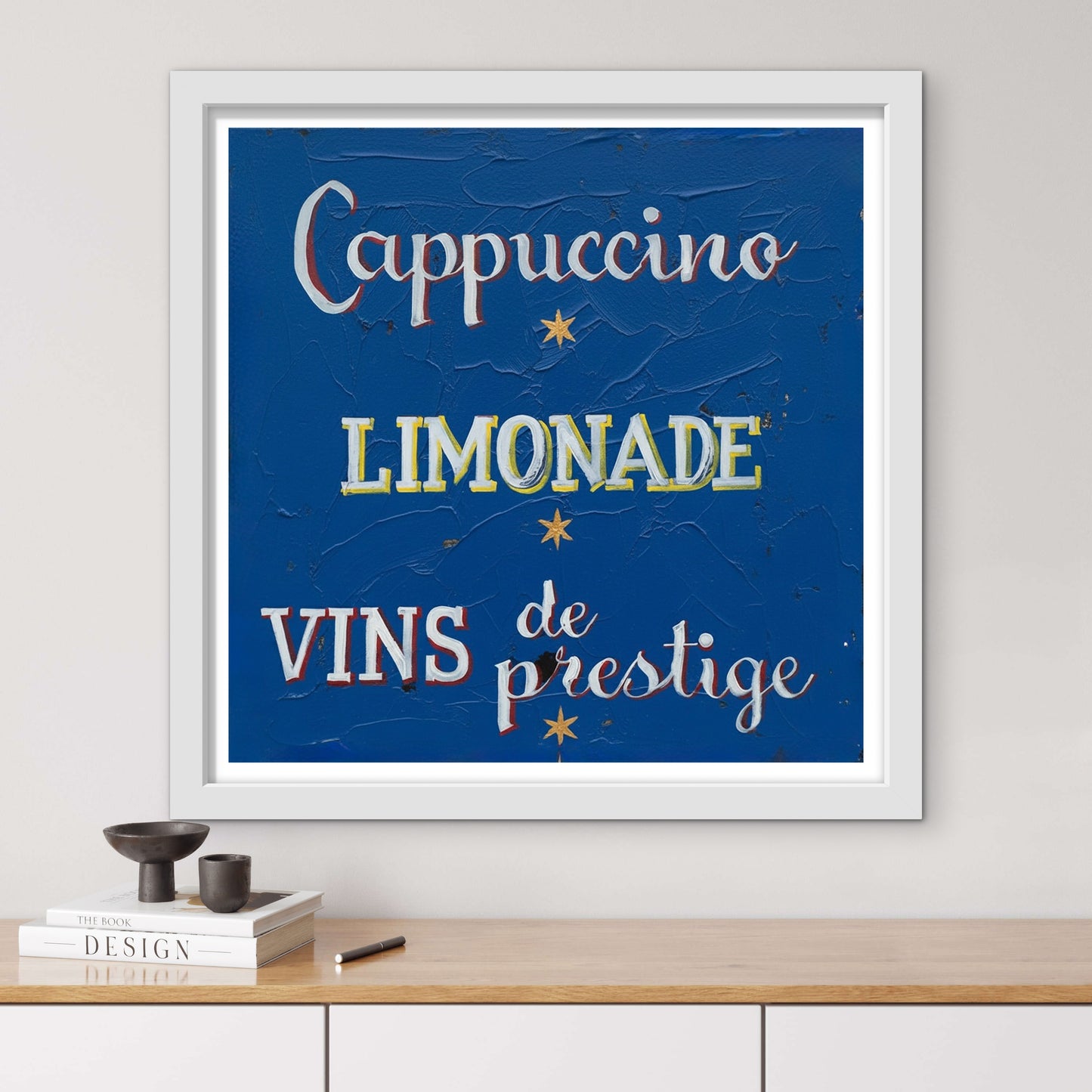 Framed artwork with text 'Cappuccino', 'Limonade', 'Vins de prestige' on a blue background, displayed on a wall.