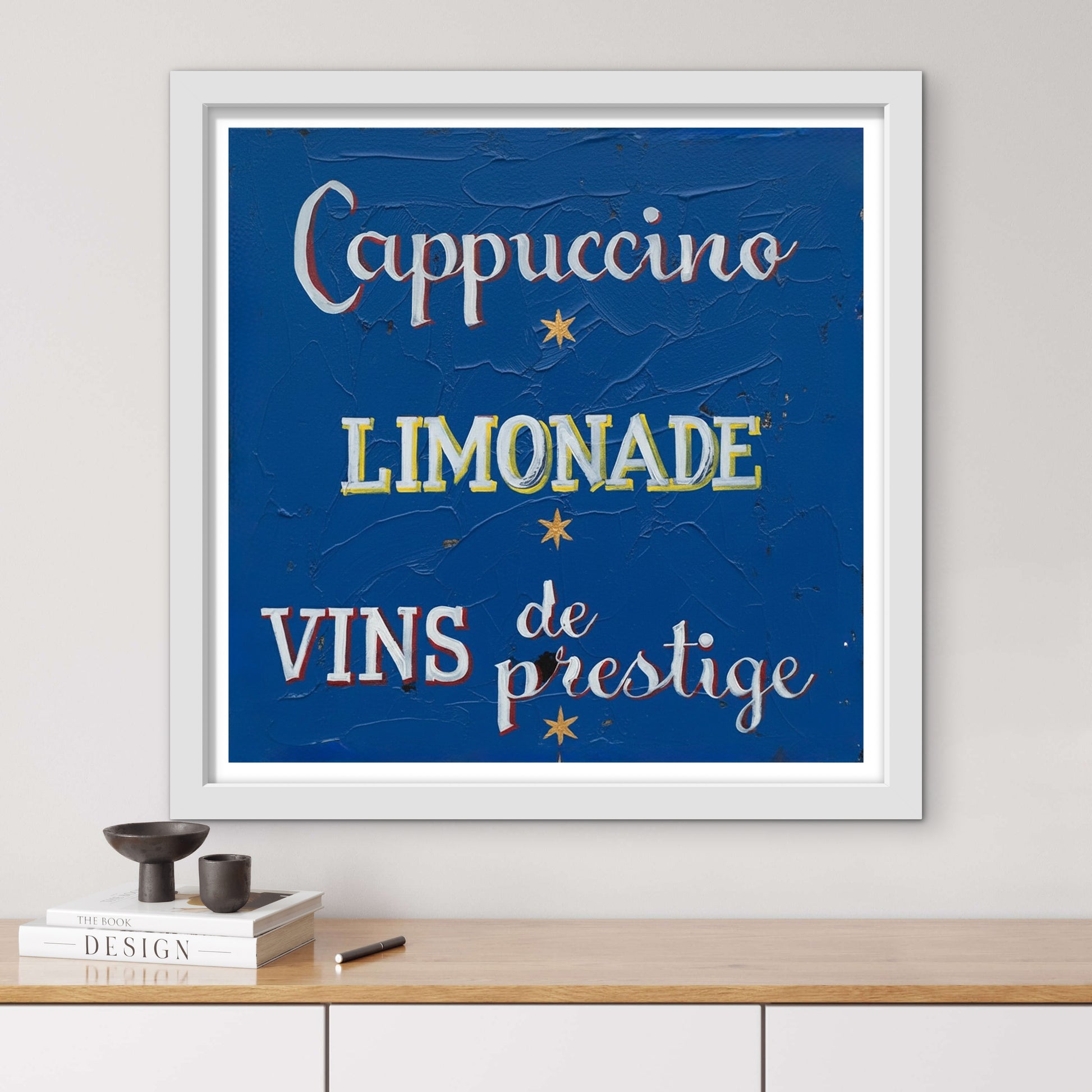 Framed artwork with text 'Cappuccino', 'Limonade', 'Vins de prestige' on a blue background, displayed on a wall.