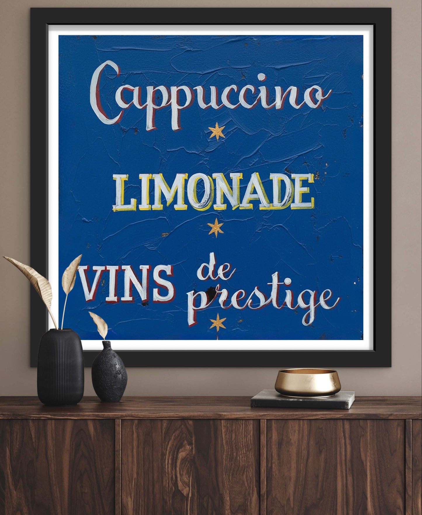 Framed artwork with text 'Cappuccino', 'Limonade', 'Vins de prestige' on a blue background, displayed on a wooden surface.