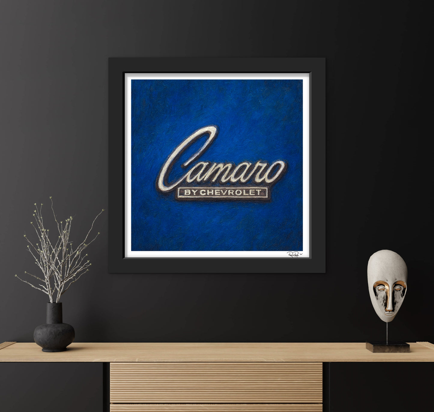 Framed artwork with 'Camaro by Chevrolet' logo on a blue background, displayed on a dark wall with decorative items.