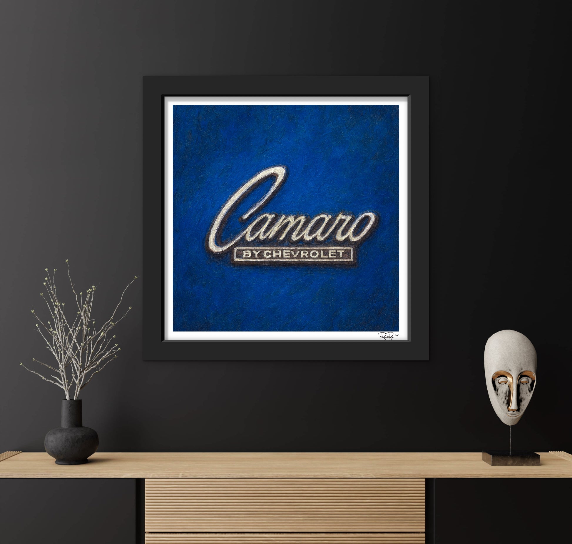 Framed artwork with 'Camaro by Chevrolet' logo on a blue background, displayed on a dark wall with decorative items.