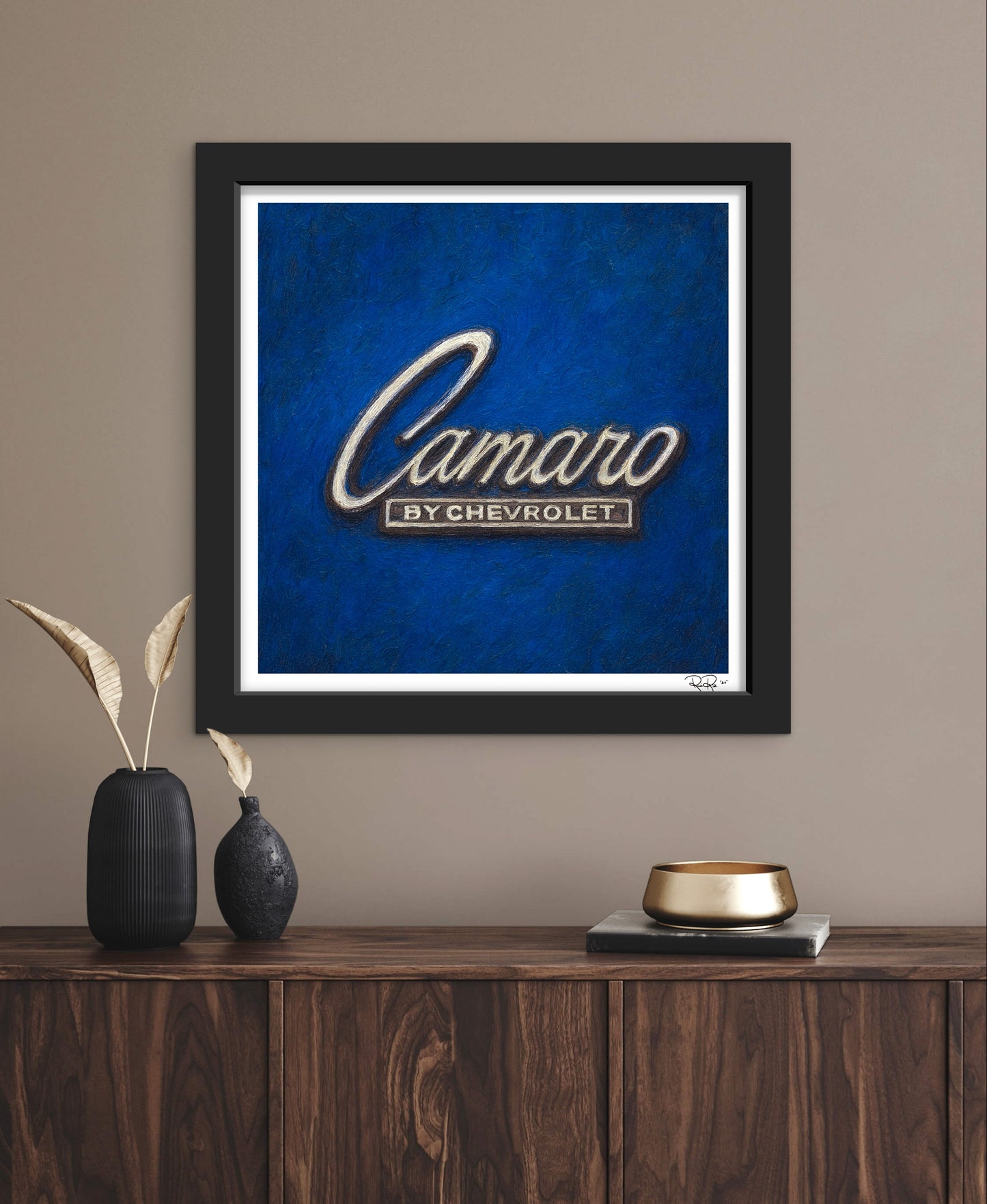Framed artwork with 'Camaro by Chevrolet' logo on a blue background, displayed on a wooden shelf.