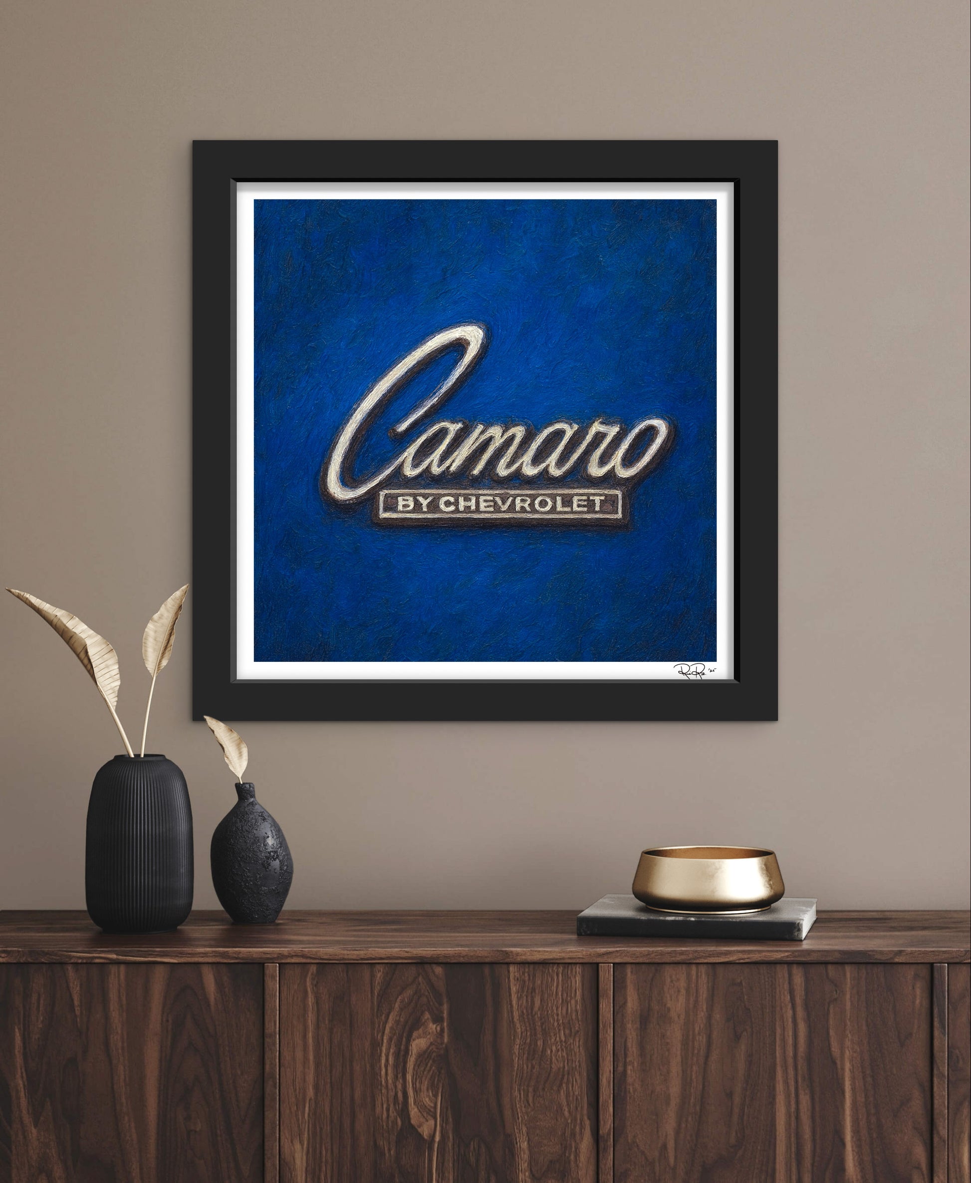 Framed artwork with 'Camaro by Chevrolet' logo on a blue background, displayed on a wooden shelf.
