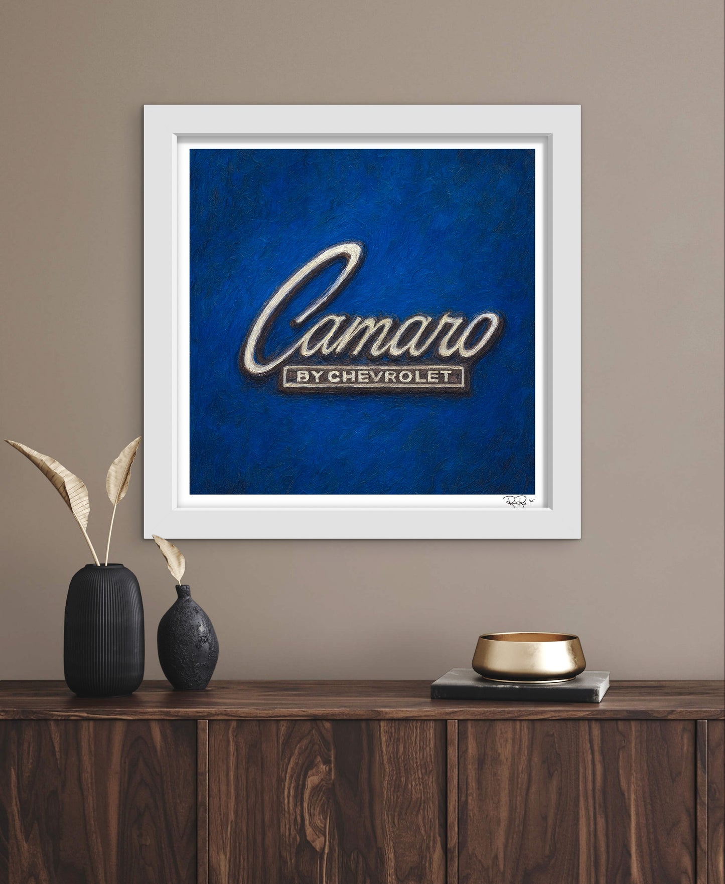 Framed artwork of the 'Camaro by Chevrolet' logo on a blue background, displayed on a wooden shelf.