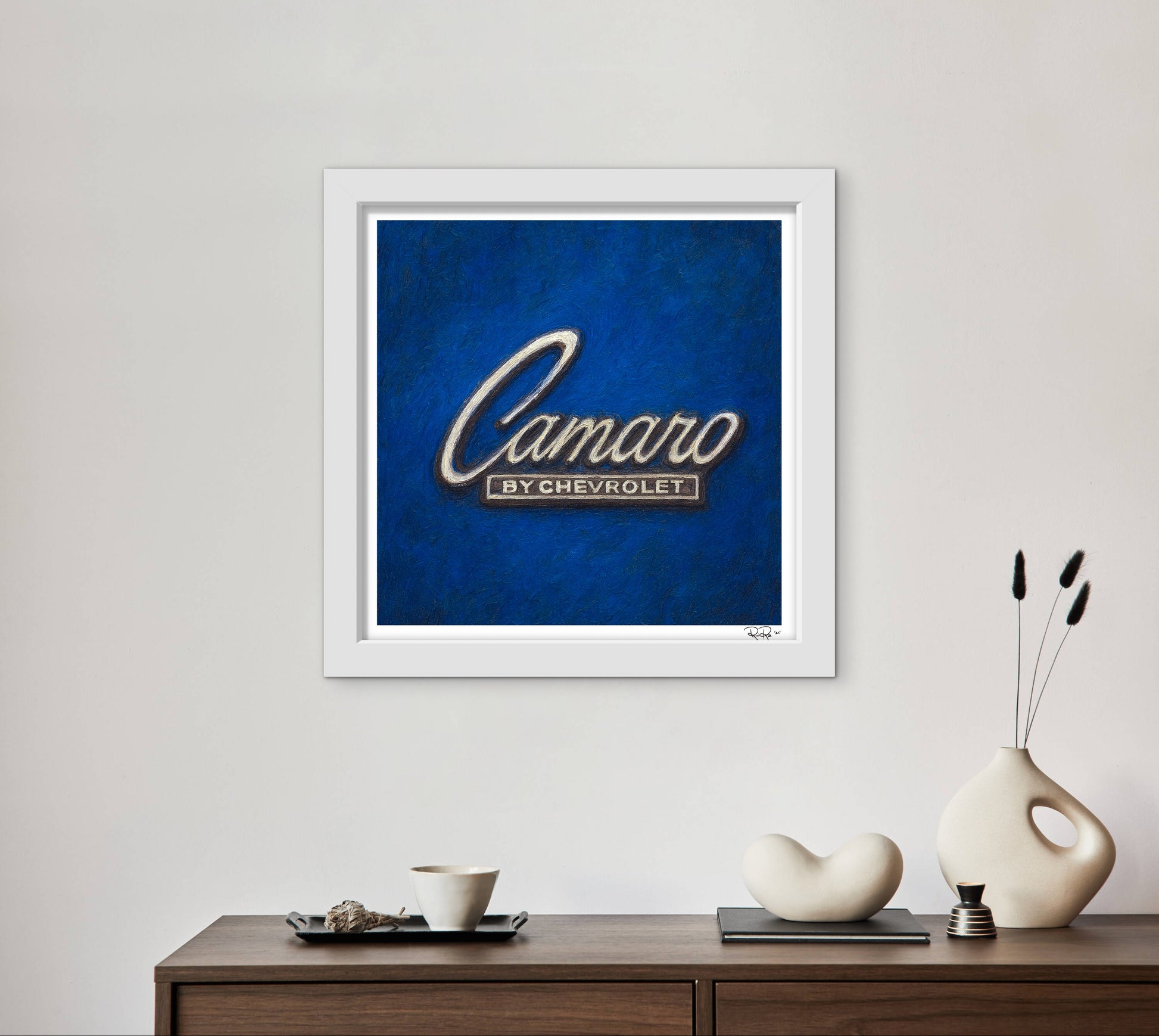 Framed artwork with 'Camaro by Chevrolet' on a blue background, displayed on a wall above a wooden console table.