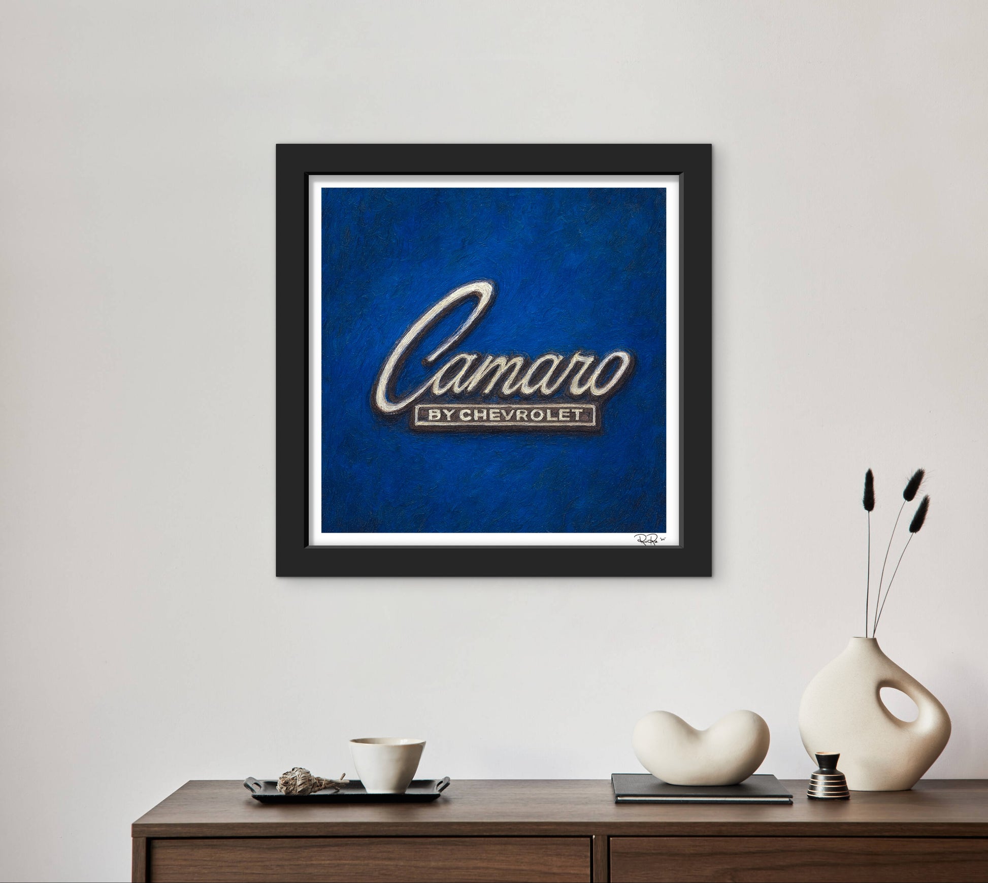 Framed artwork with 'Camaro by Chevrolet' on a blue background, displayed on a wall above a wooden console table.