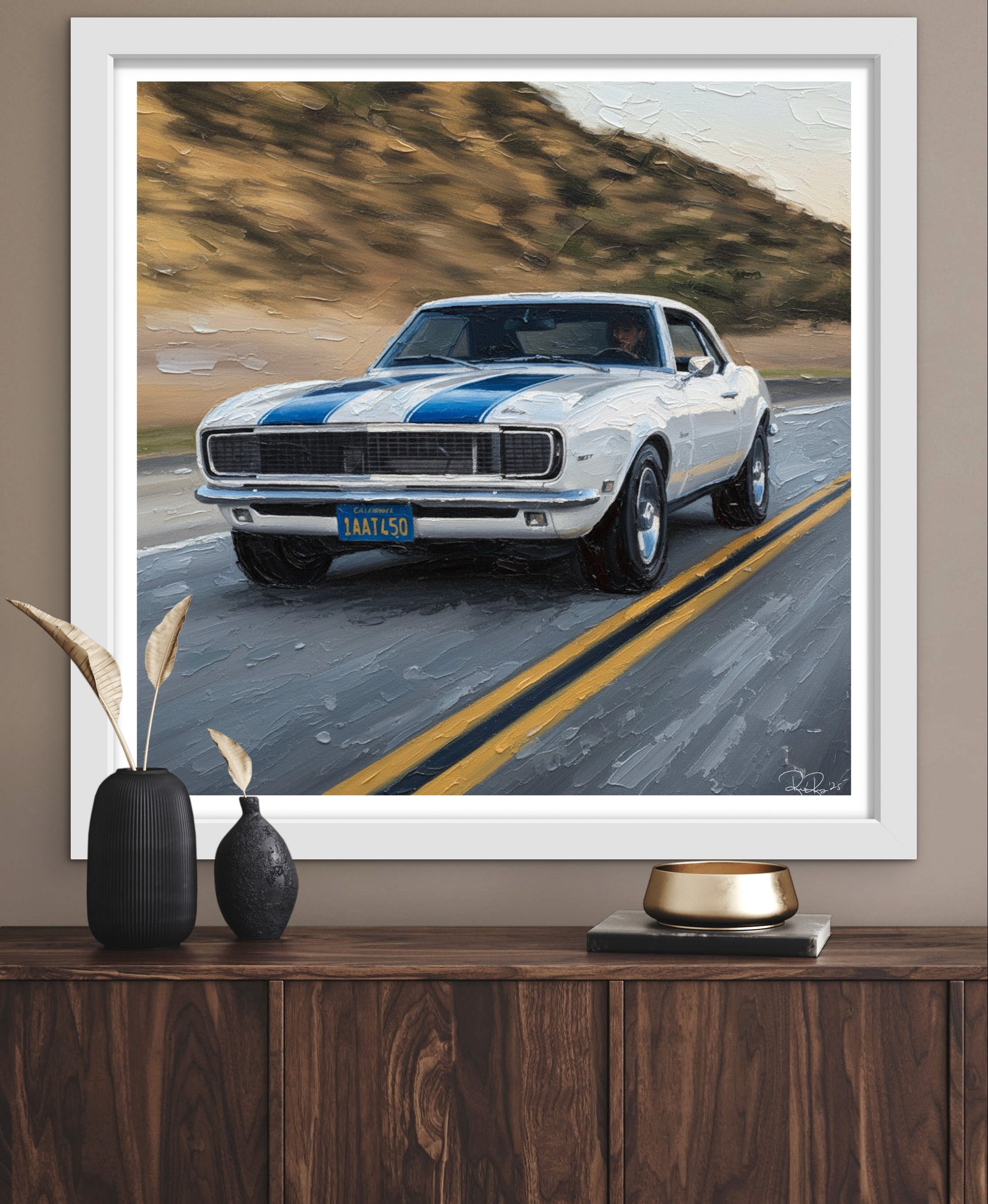 Framed artwork of a classic car on a road with decorative items below.