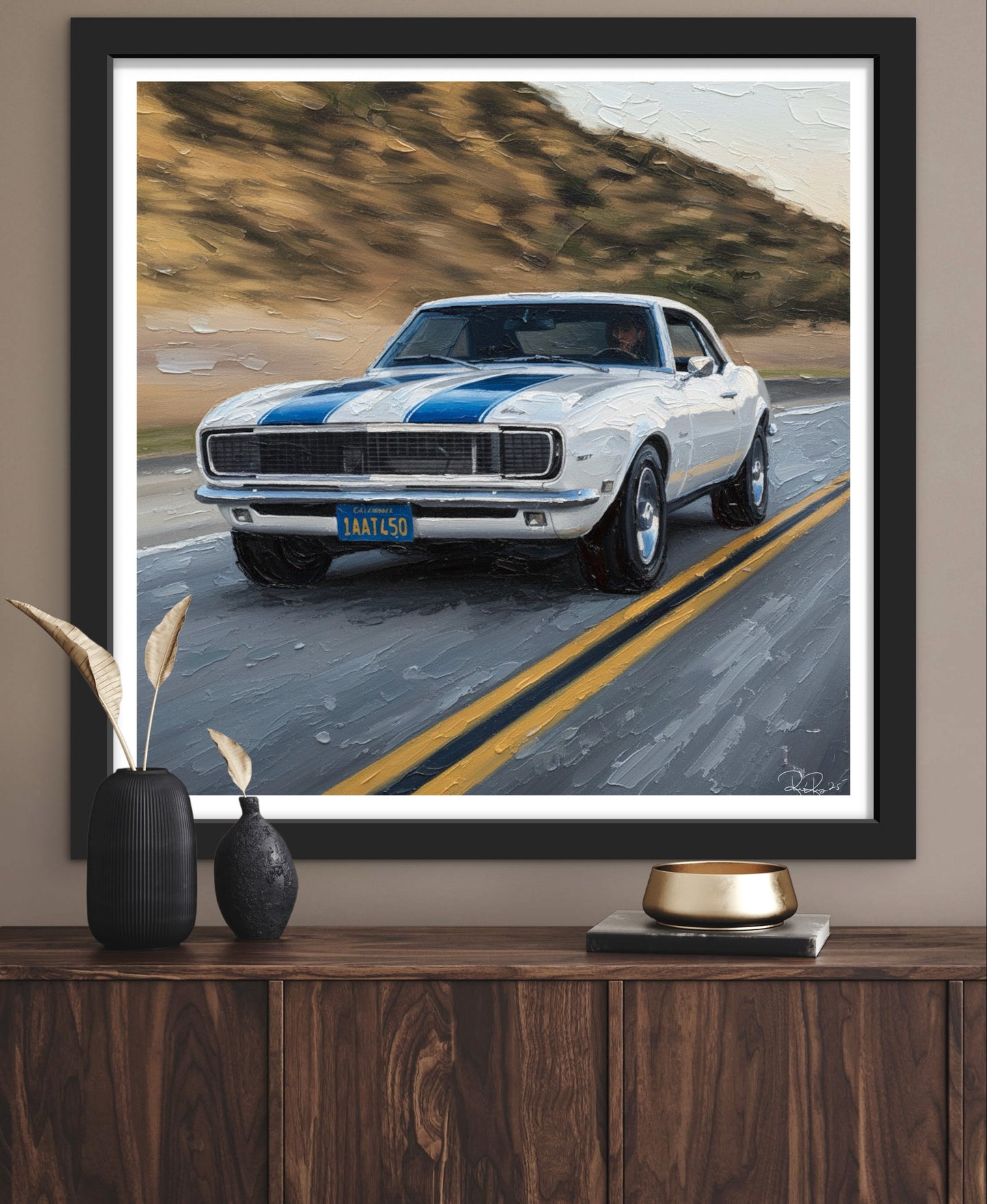 Framed artwork of a classic car on a road with decorative items below.