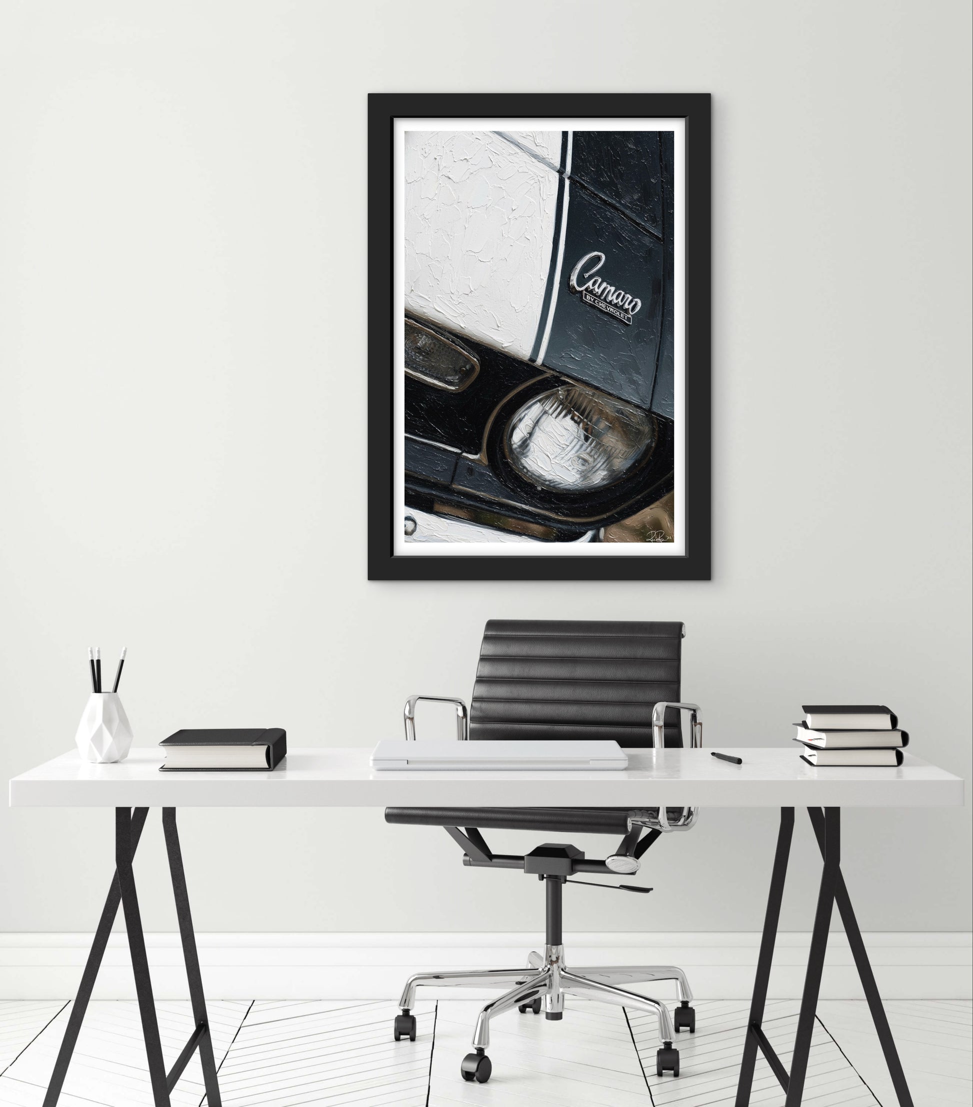 Framed artwork of a car's headlight on a white wall above a desk with office furniture.
