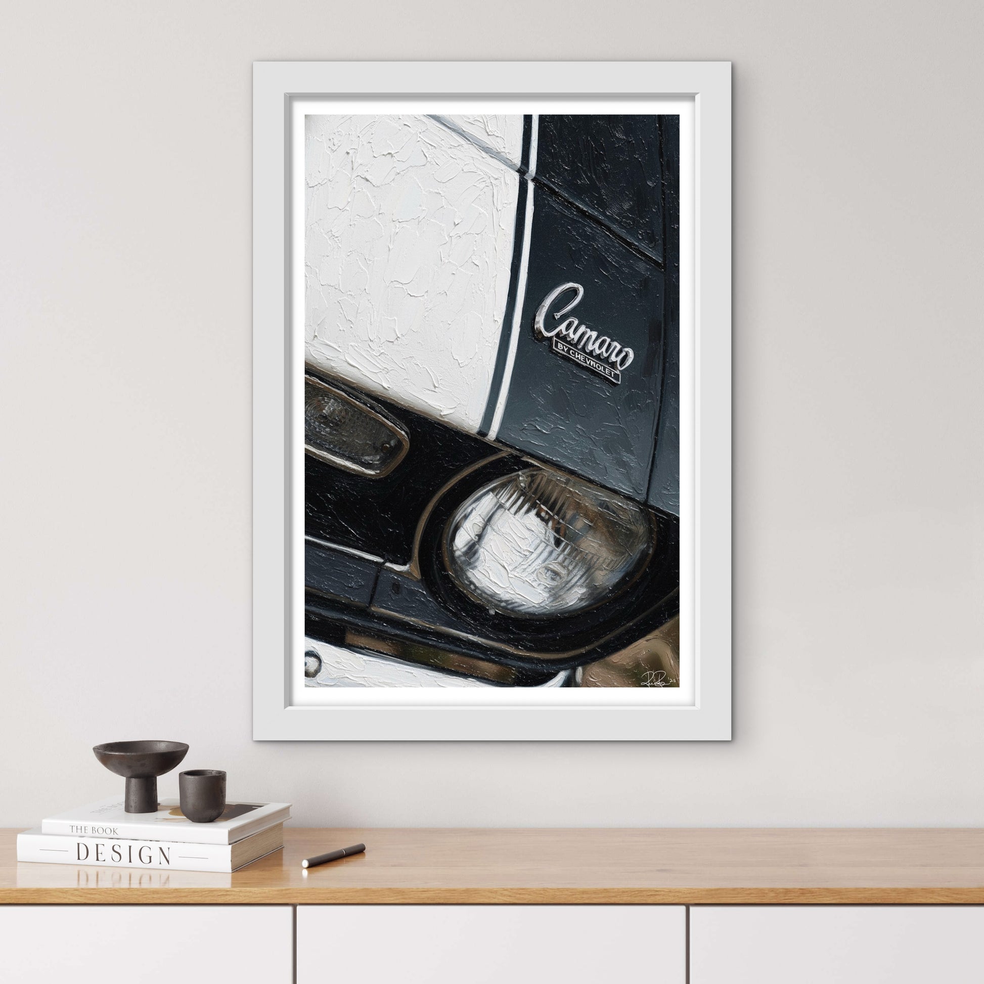Framed artwork of a car headlight with 'Camaro' branding on a wall above a wooden shelf.