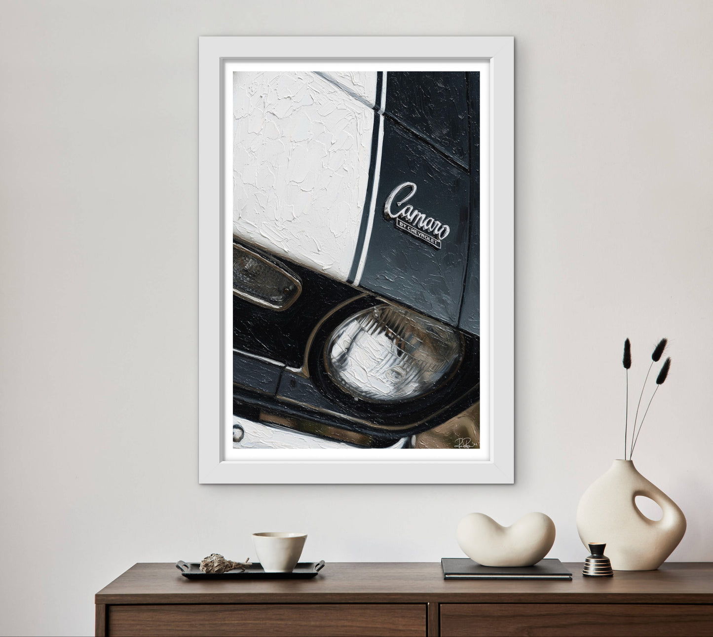 Framed artwork of a car headlight with 'Camaro' branding on a wall above a wooden console table.