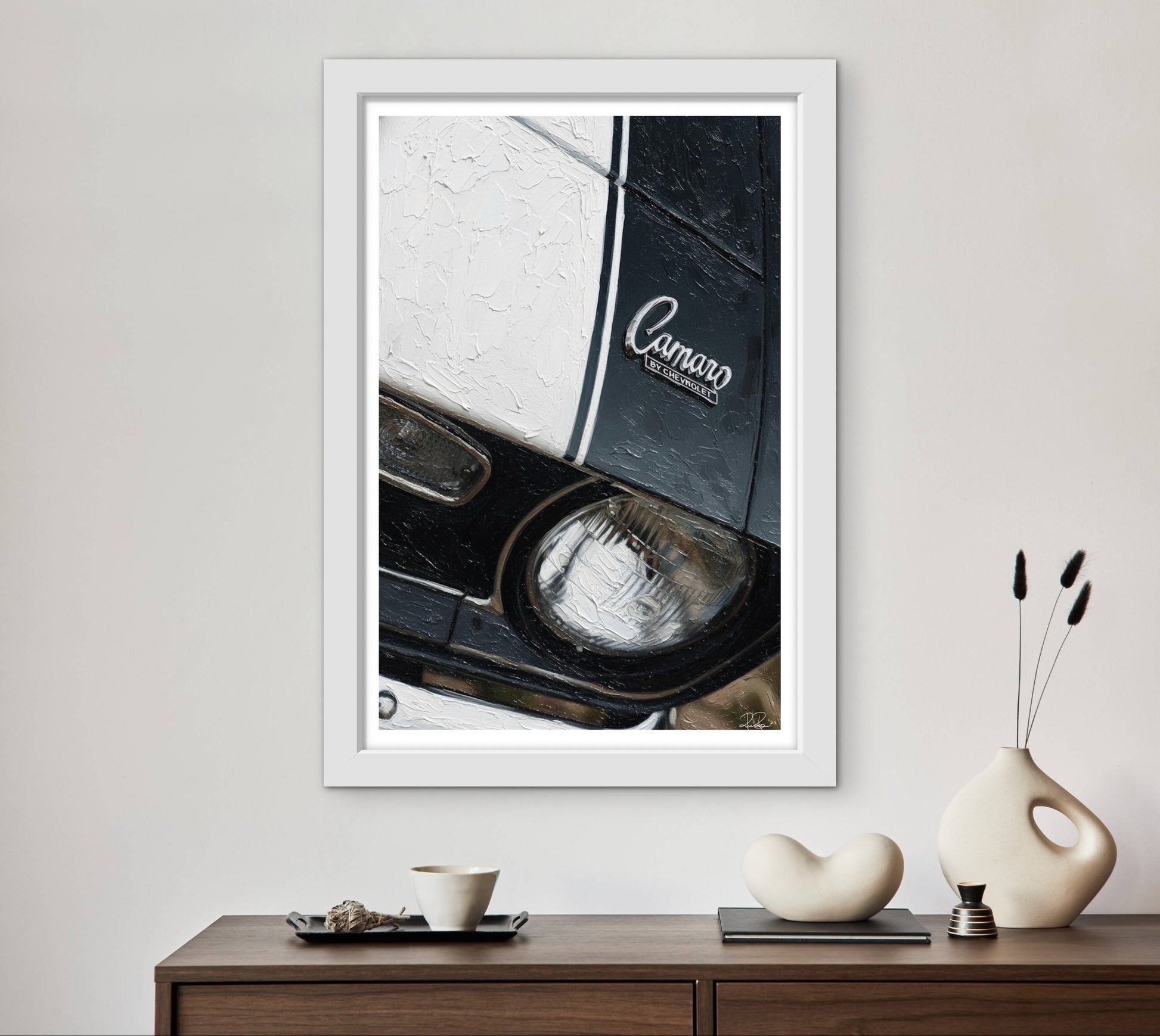 Framed artwork of a car headlight with 'Camaro' branding on a wall above a wooden console table.