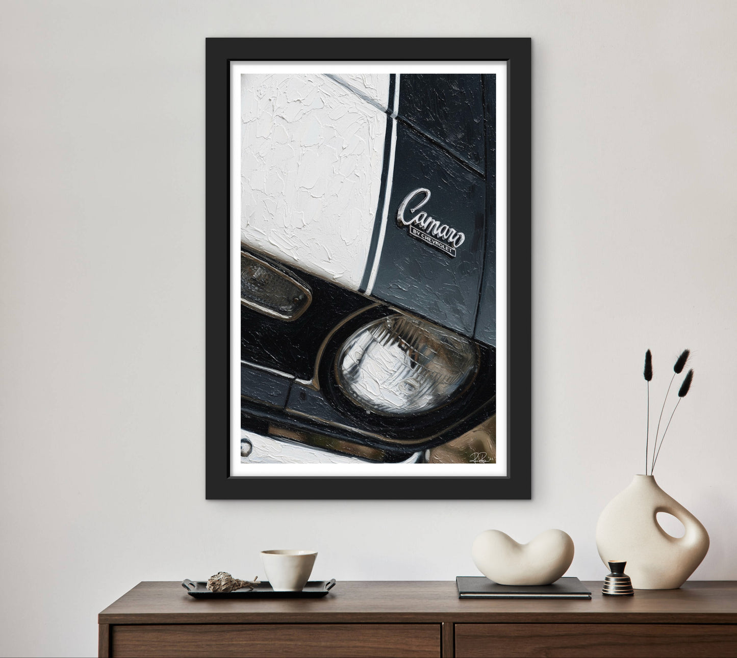 Framed picture of a car headlight with 'Camaro' branding on a wall above a wooden console table.