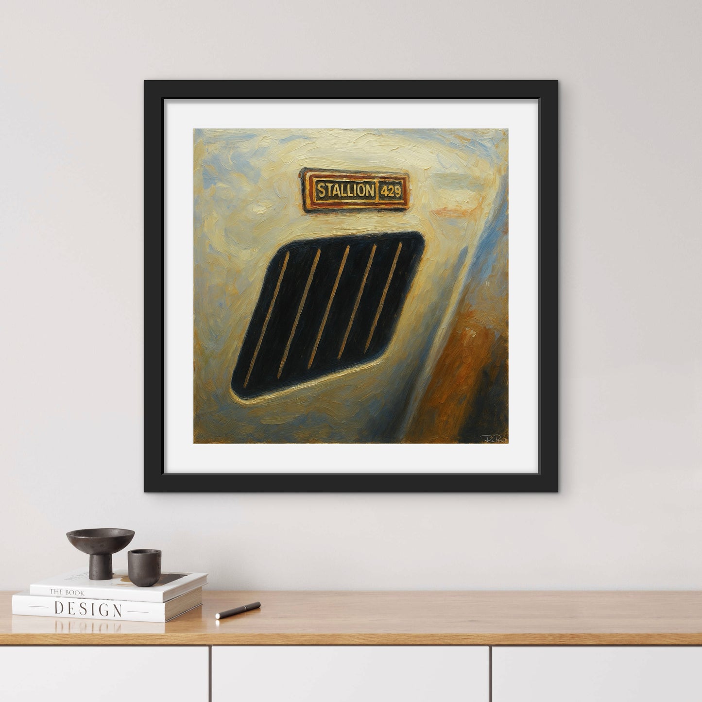 Framed artwork of a car grille with 'STALLION 428' on a white wall above a wooden shelf.