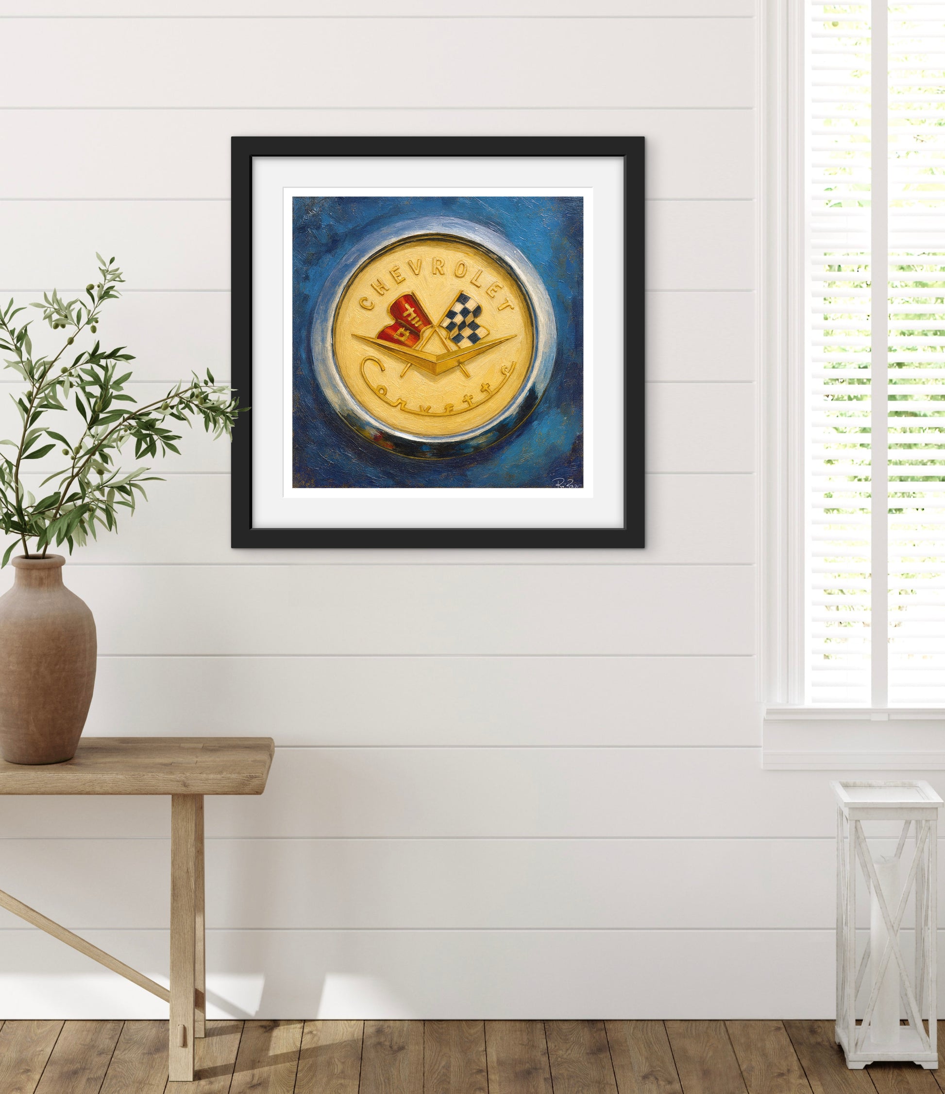 Framed artwork of a Chevrolet logo on a blue background in a room with a wooden table and plant.