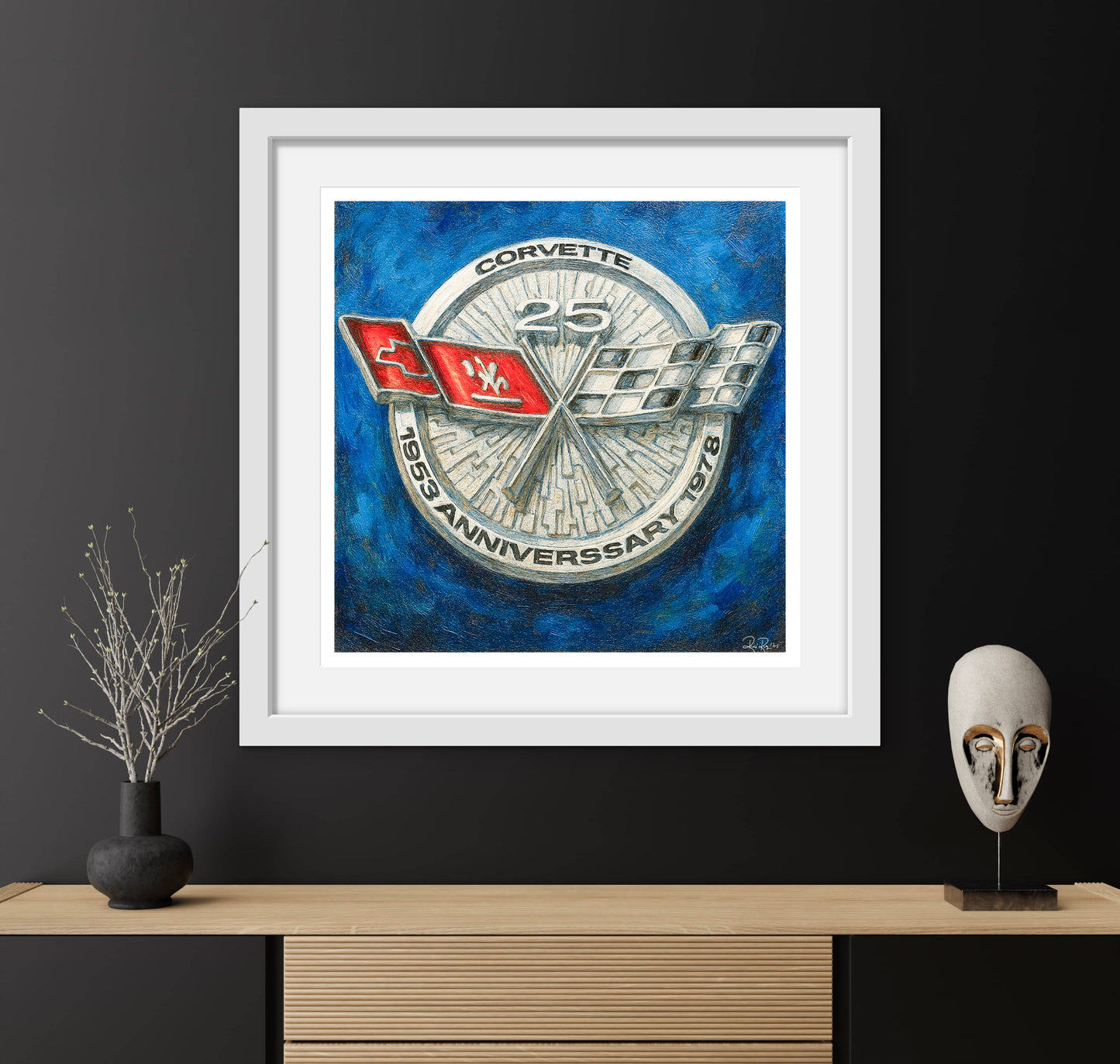 Framed artwork of a Corvette logo on a blue background, displayed on a wooden shelf with decorative items.
