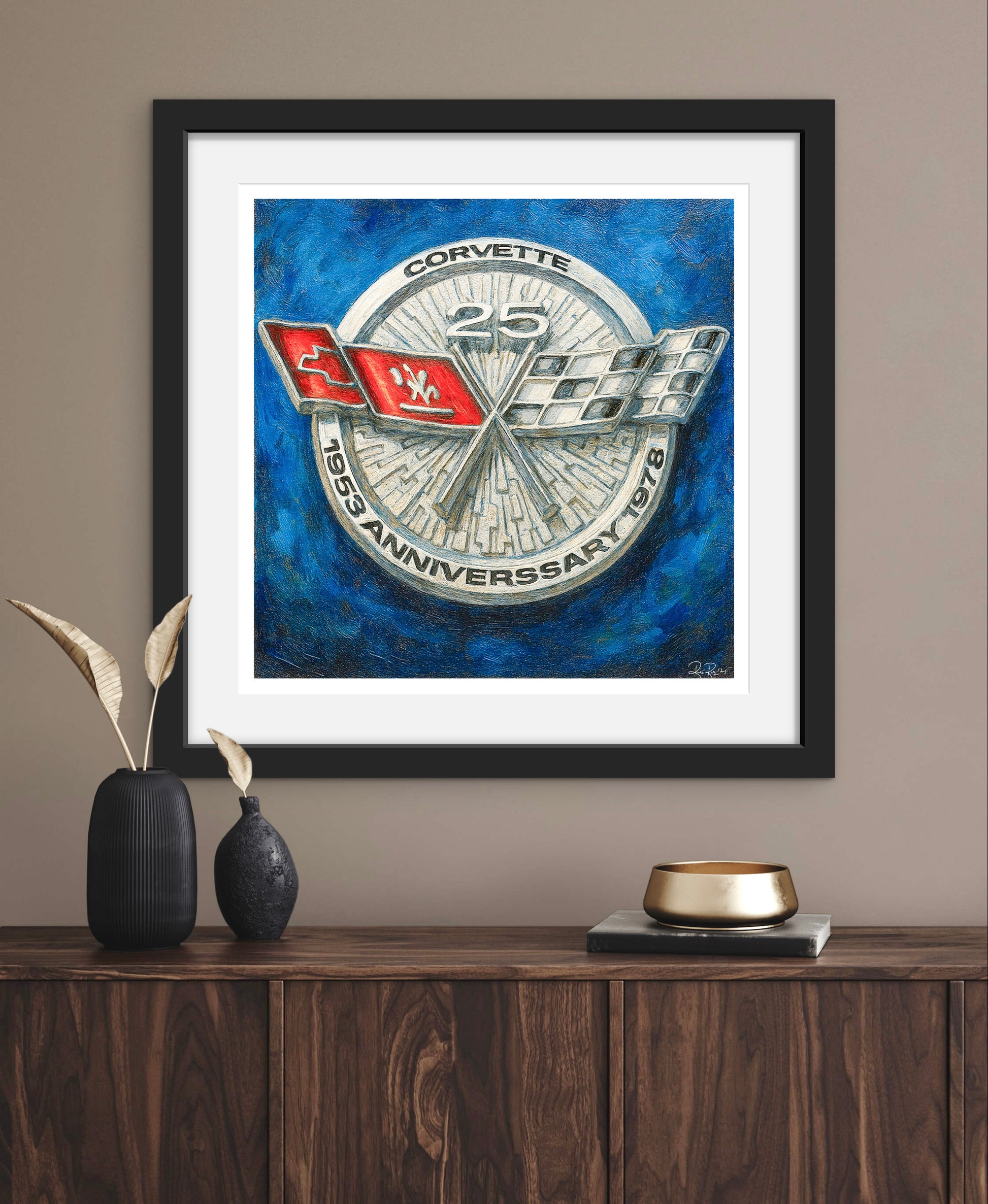 Framed artwork of a Corvette logo on a blue background, displayed on a wooden surface.
